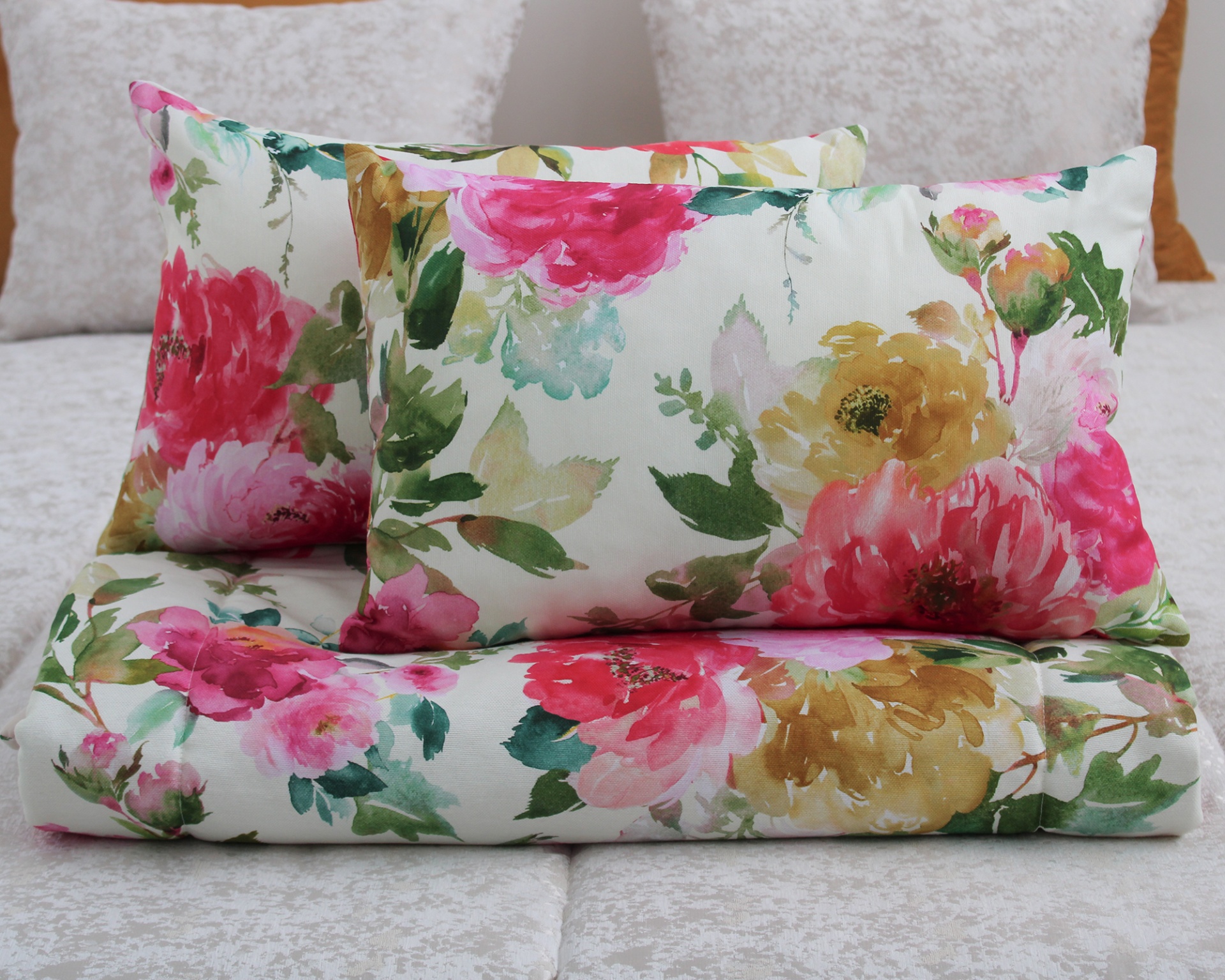 Almofadas e manta com padrão floral colorido sobre cama cinza claro.