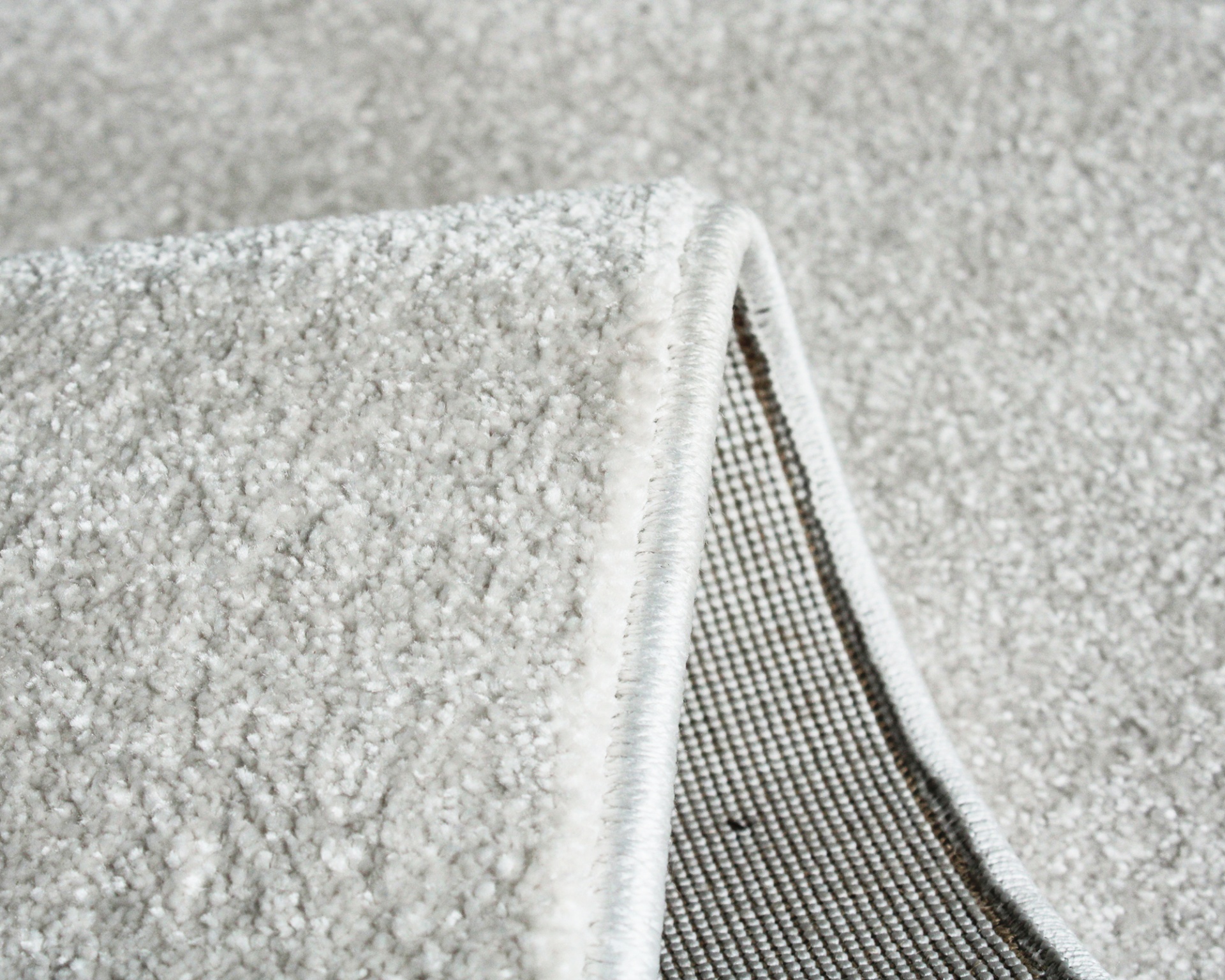 Tapete cinzento claro felpudo com bordas rematadas e verso com padrão quadriculado