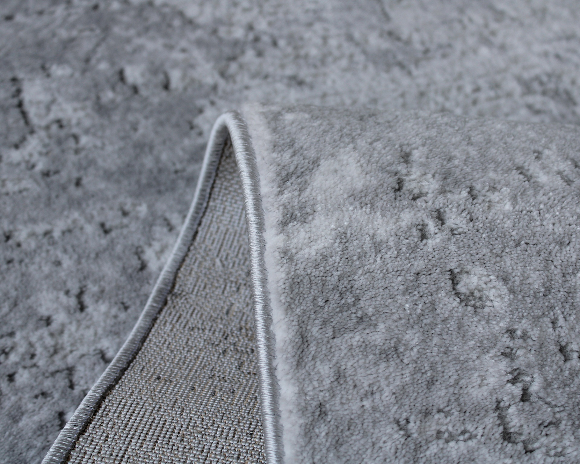 Tapete cinza claro felpudo com borda fechada sobre piso cinza.