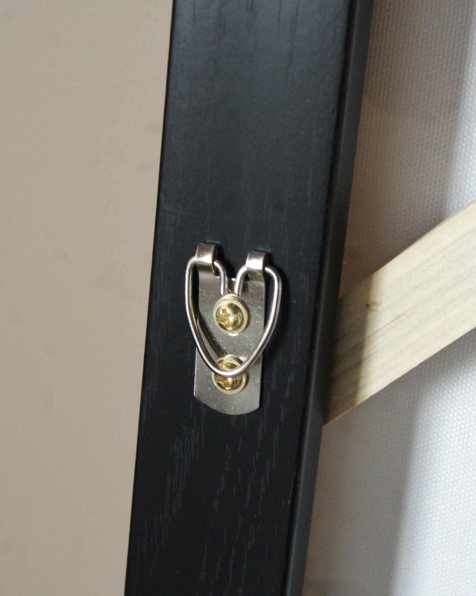 Suporte metálico para pendurar em moldura de madeira preta com tela branca ao fundo