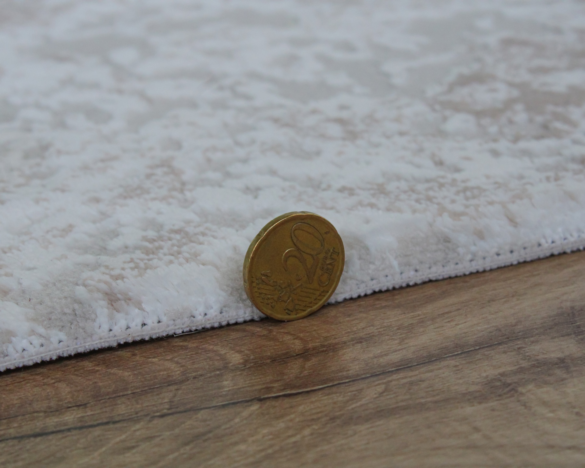Tapete branco texturizado com moeda dourada de 20 centavos em cima de chão de madeira