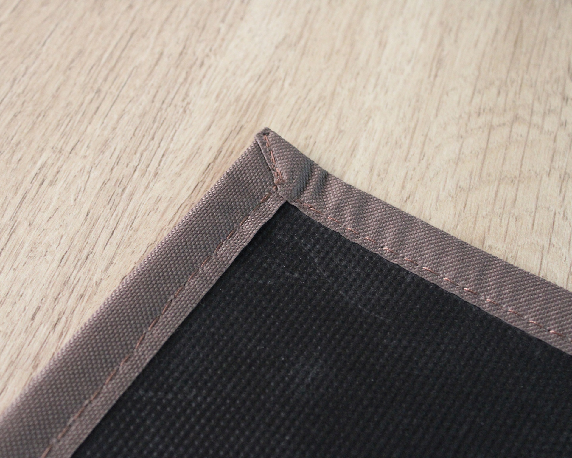 Canto de tapete com base preta e borda castanha sobre chão de madeira clara.