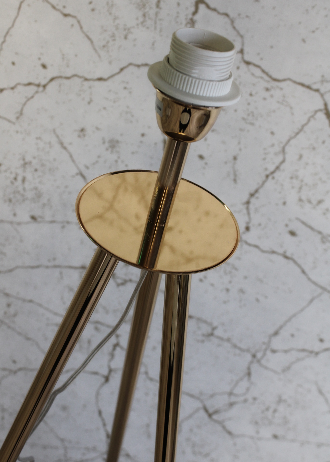 Suporte de lâmpada dourado com soquete branco sobre parede clara fissurada