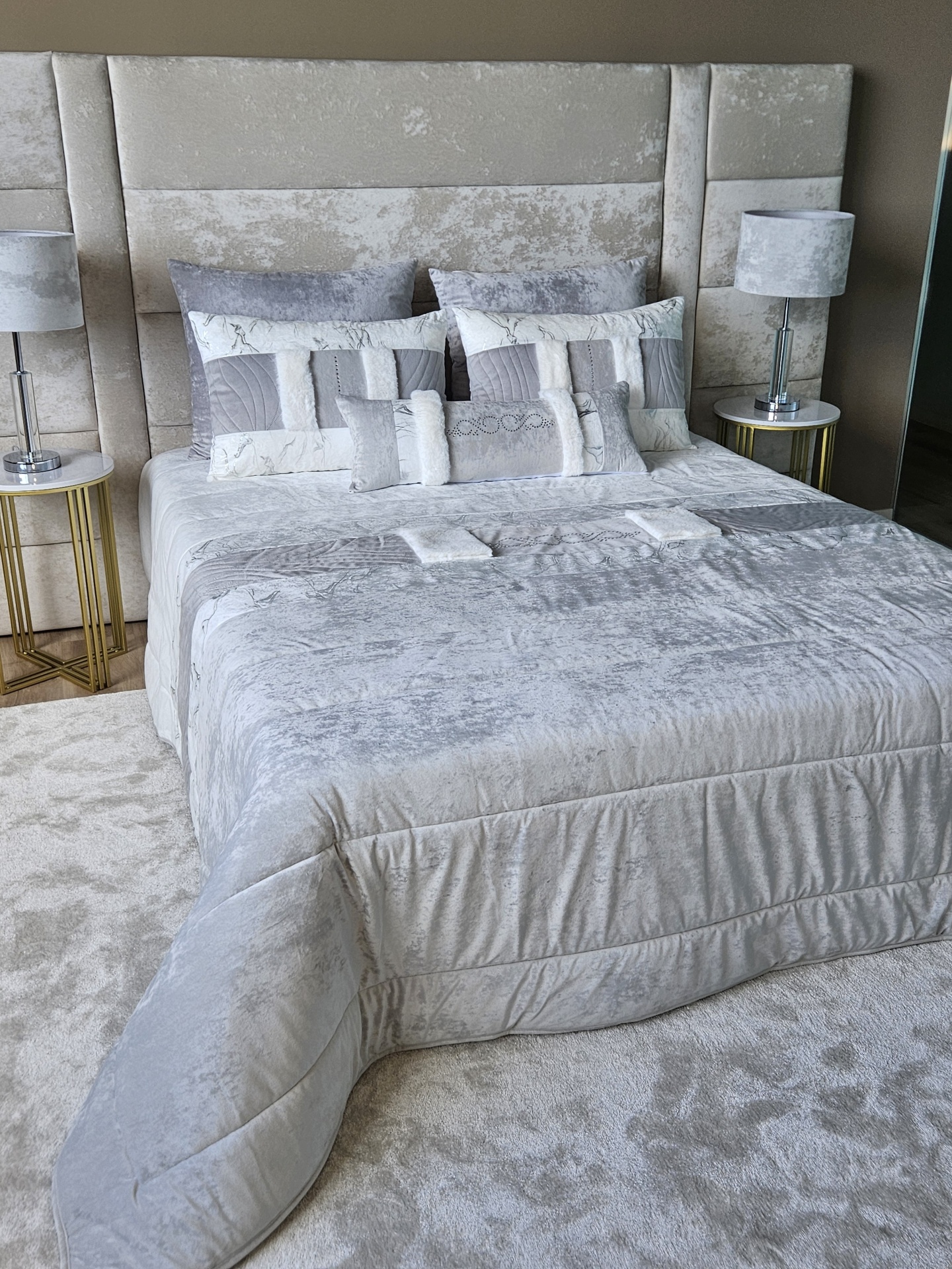 Edredão em Veludo Ref: Nepal Cinza Cama estofada cinzenta com roupa de cama cinza e branco, duas mesas de cabeceira com candeeiros cinza.