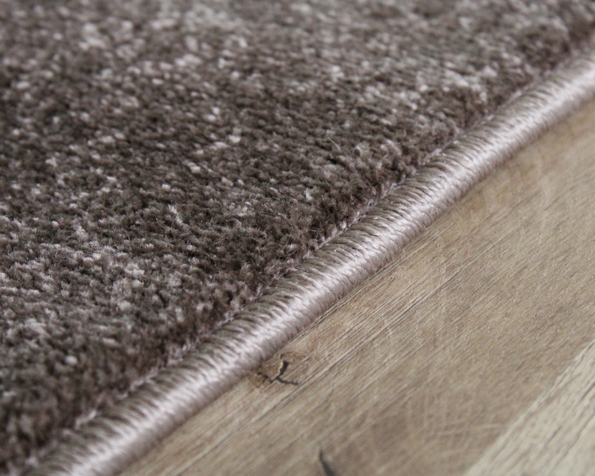 Borda de tapete cinza castanho sobre chão de madeira clara