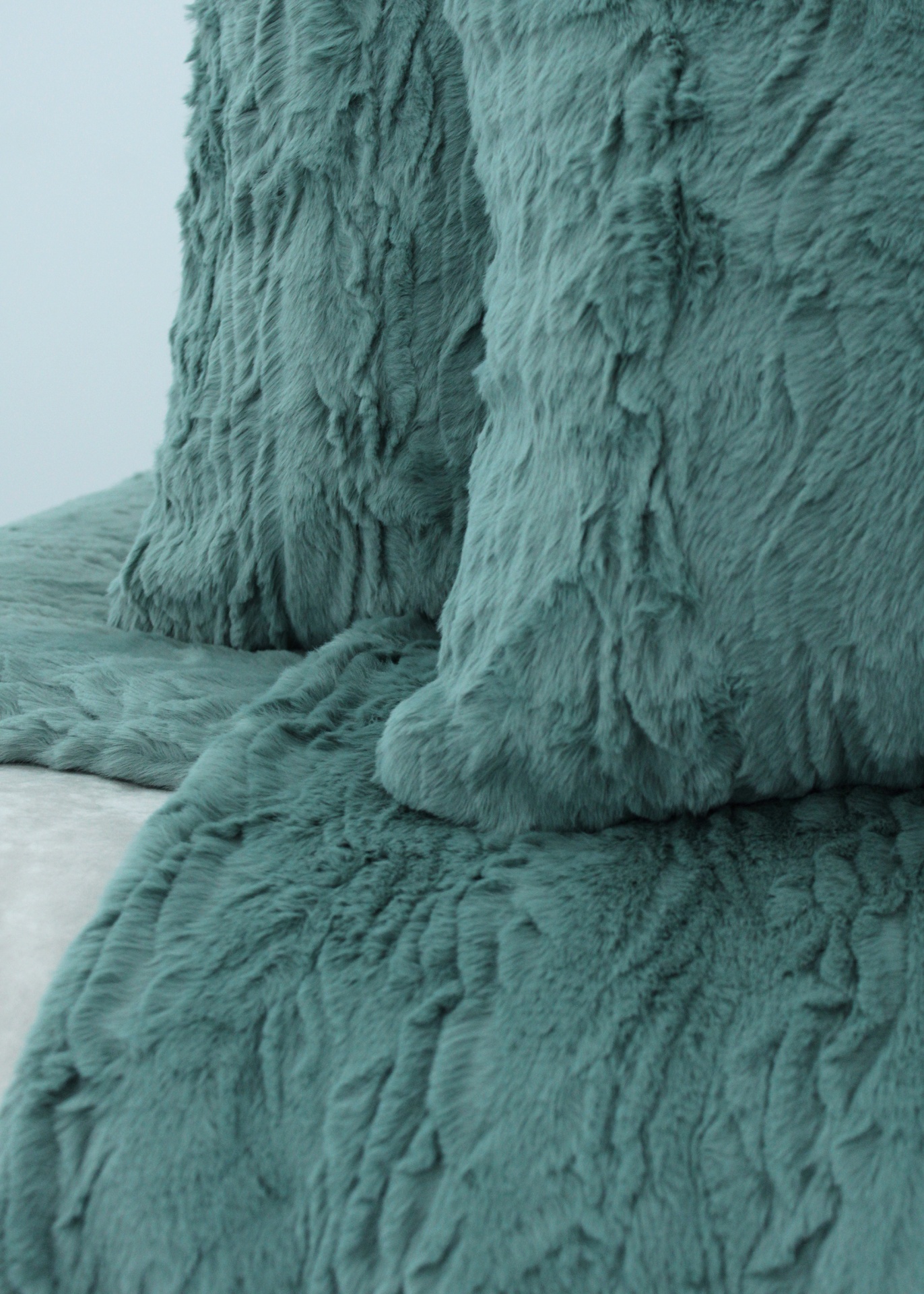 Almofadas e manta felpuda verde-azulado num sofá bege