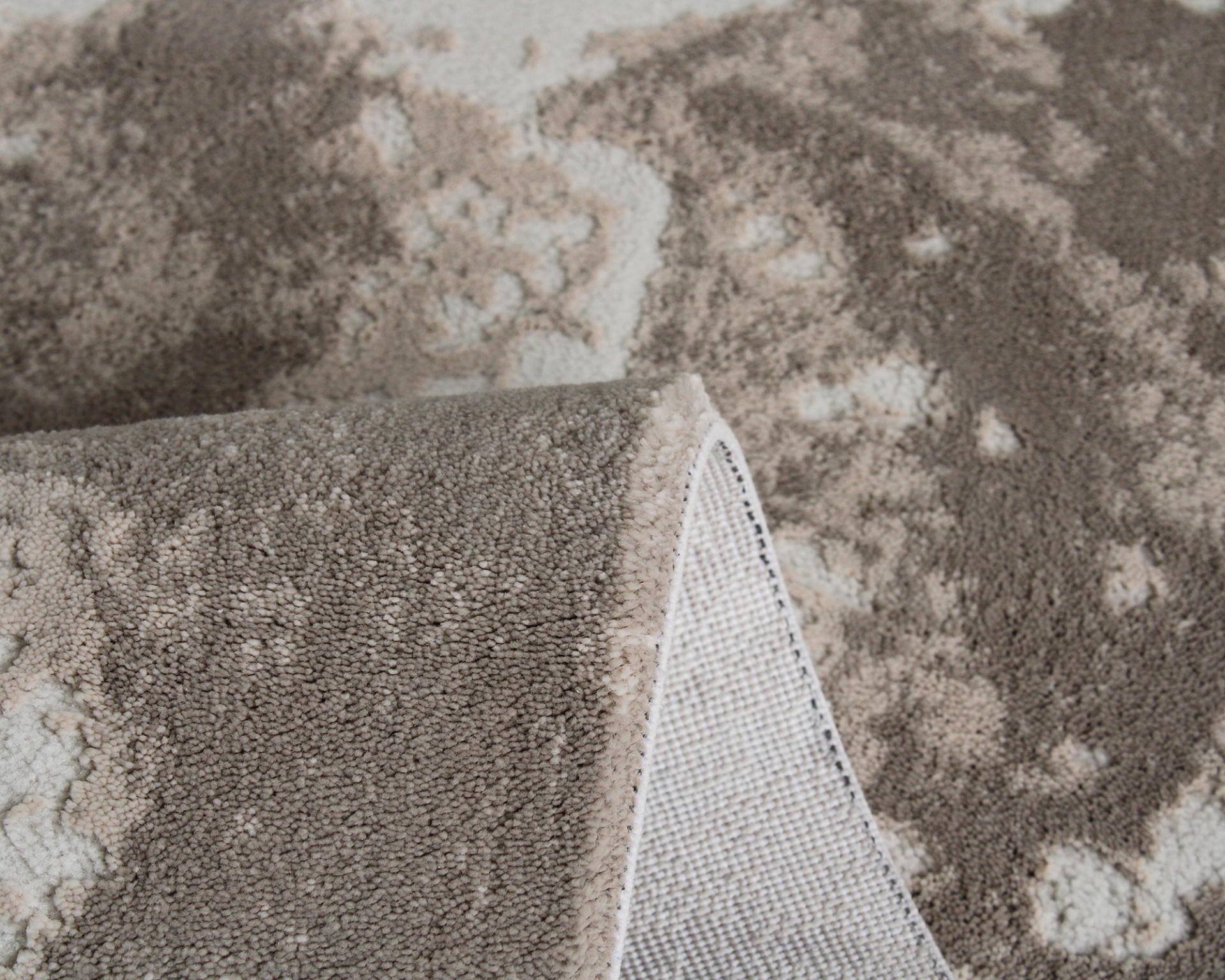 Tapete cinza e bege com textura felpuda e padrão abstrato dobrado mostrando a base antiderrapante