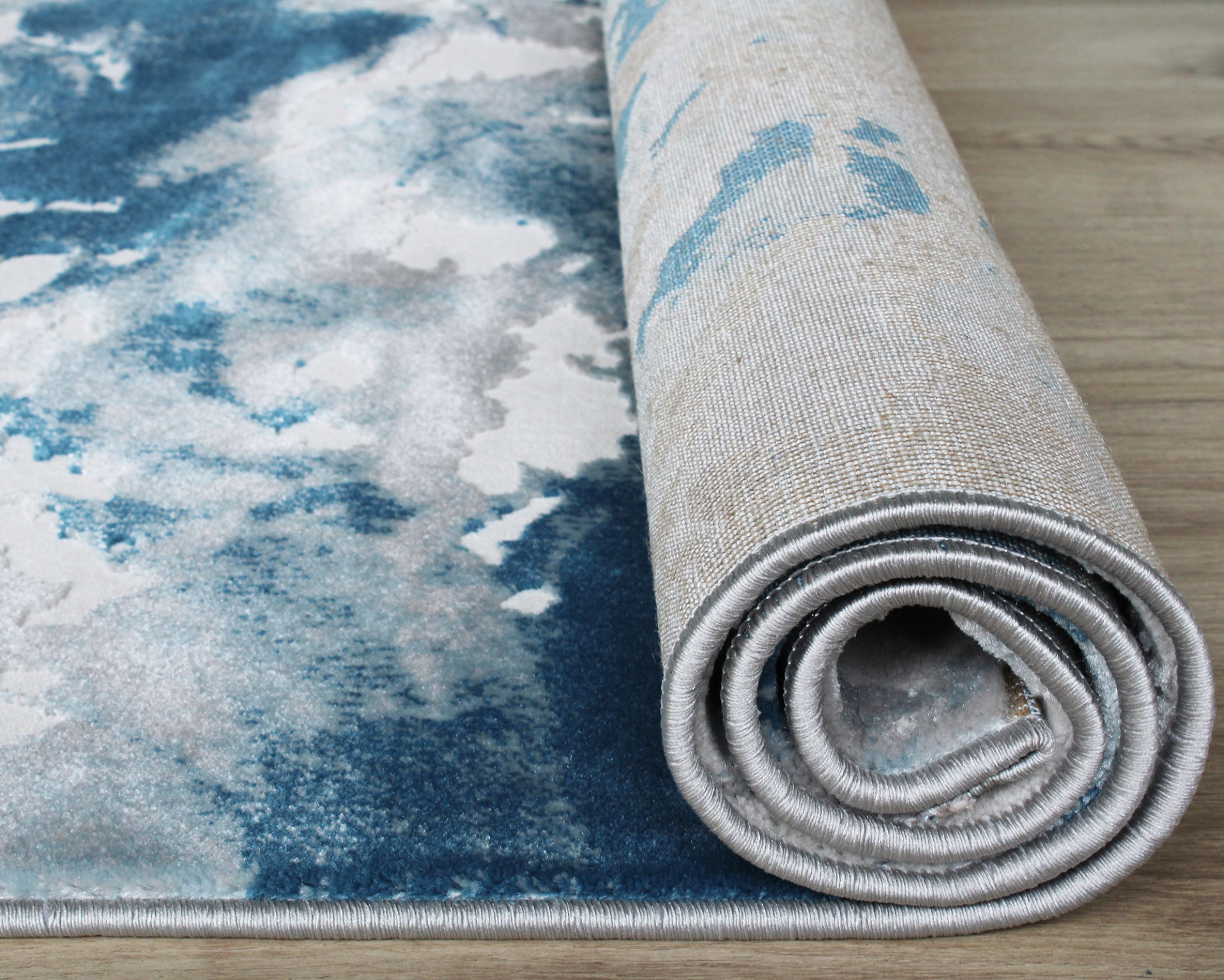 Tapete azul e branco com padrão abstrato parcialmente desenrolado sobre chão de madeira