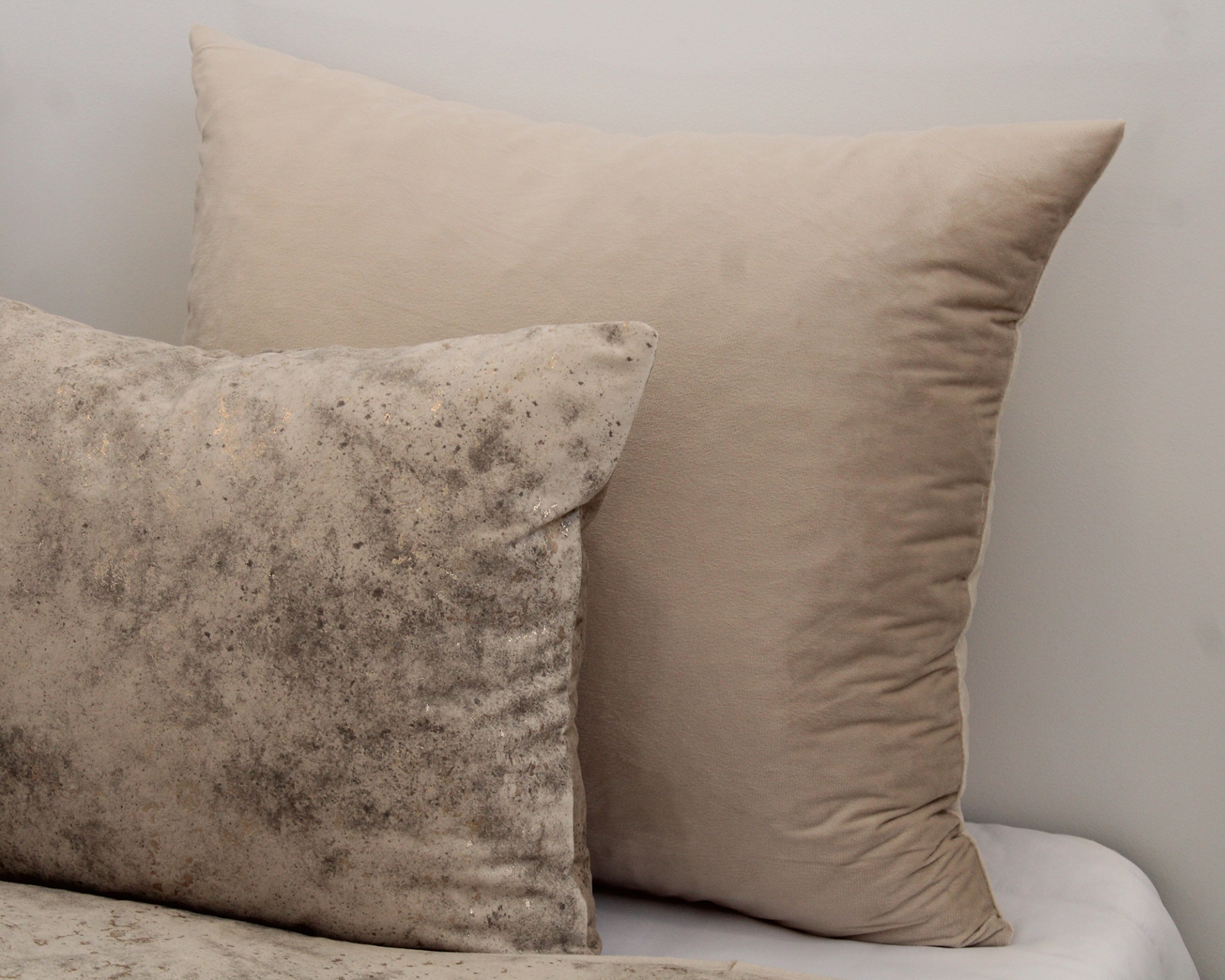 Duas almofadas decorativas em cama branca, uma bege lisa e outra com padrão marmoreado cinza e bege.