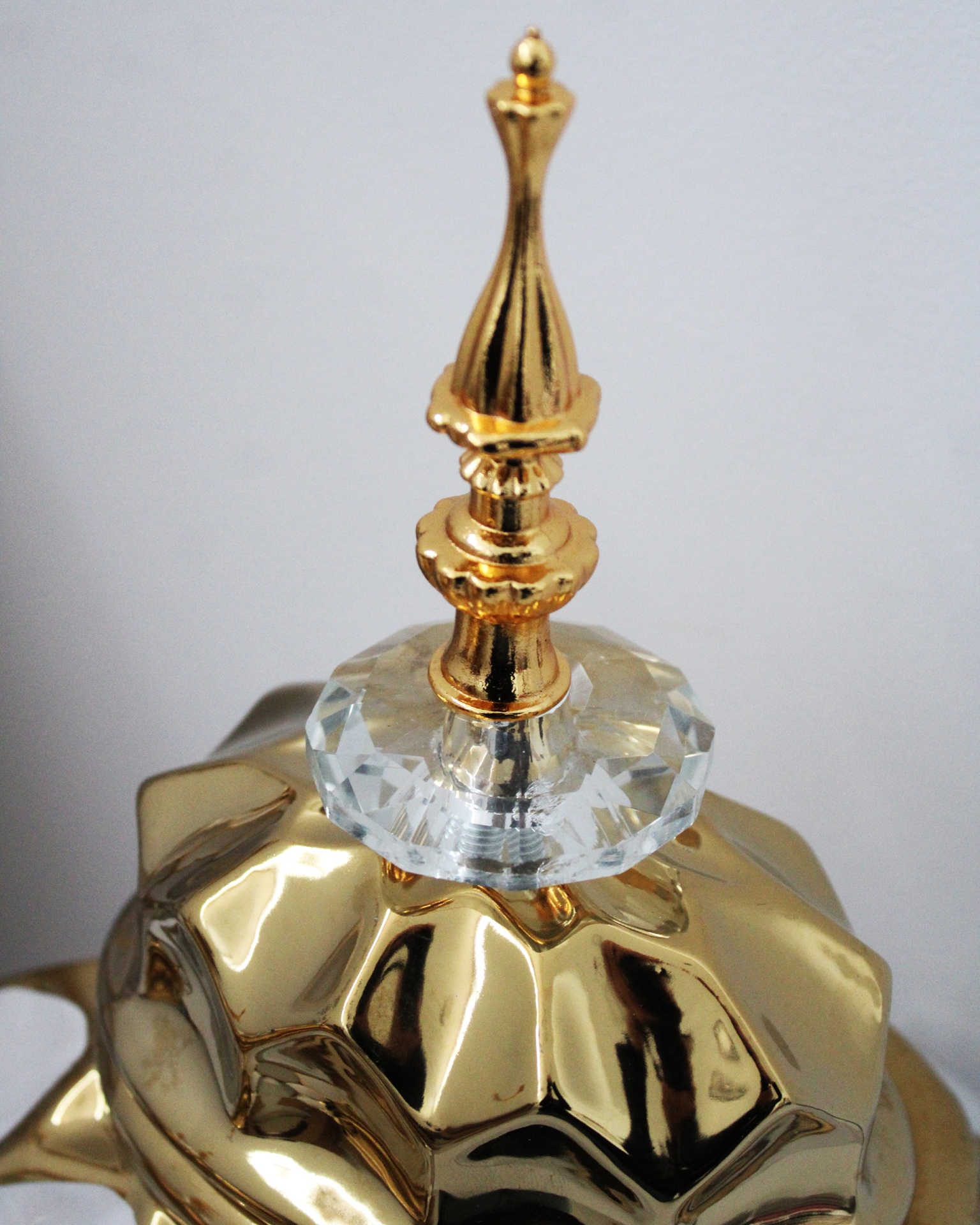 Tampa dourada facetada com puxador decorativo dourado e base de cristal.