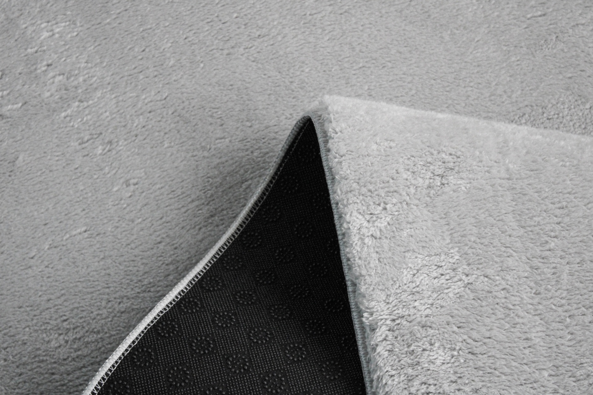 Tapete cinza claro com superfície suave e verso antiderrapante preto.