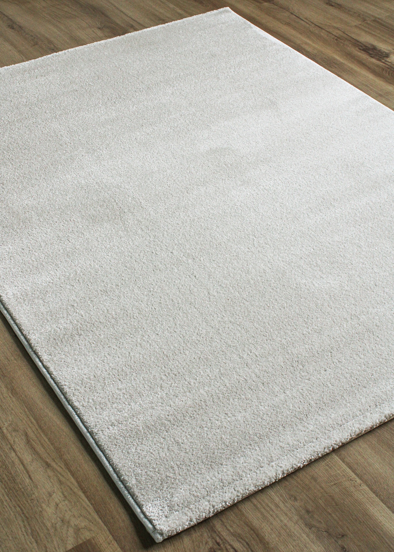 Tapete branco felpudo sobre chão de madeira clara.
