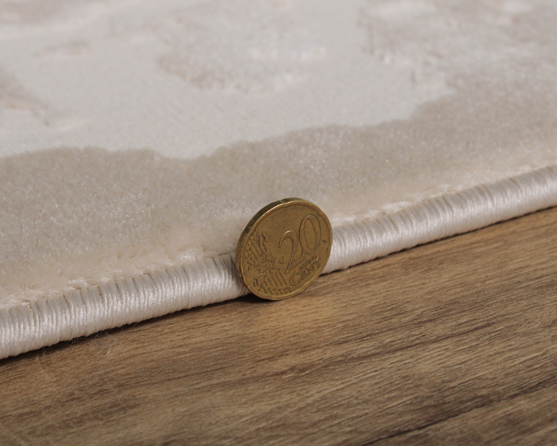 Tapete bege claro com borda cosida e moeda de 20 cêntimos para mostrar espessura sobre chão de madeira