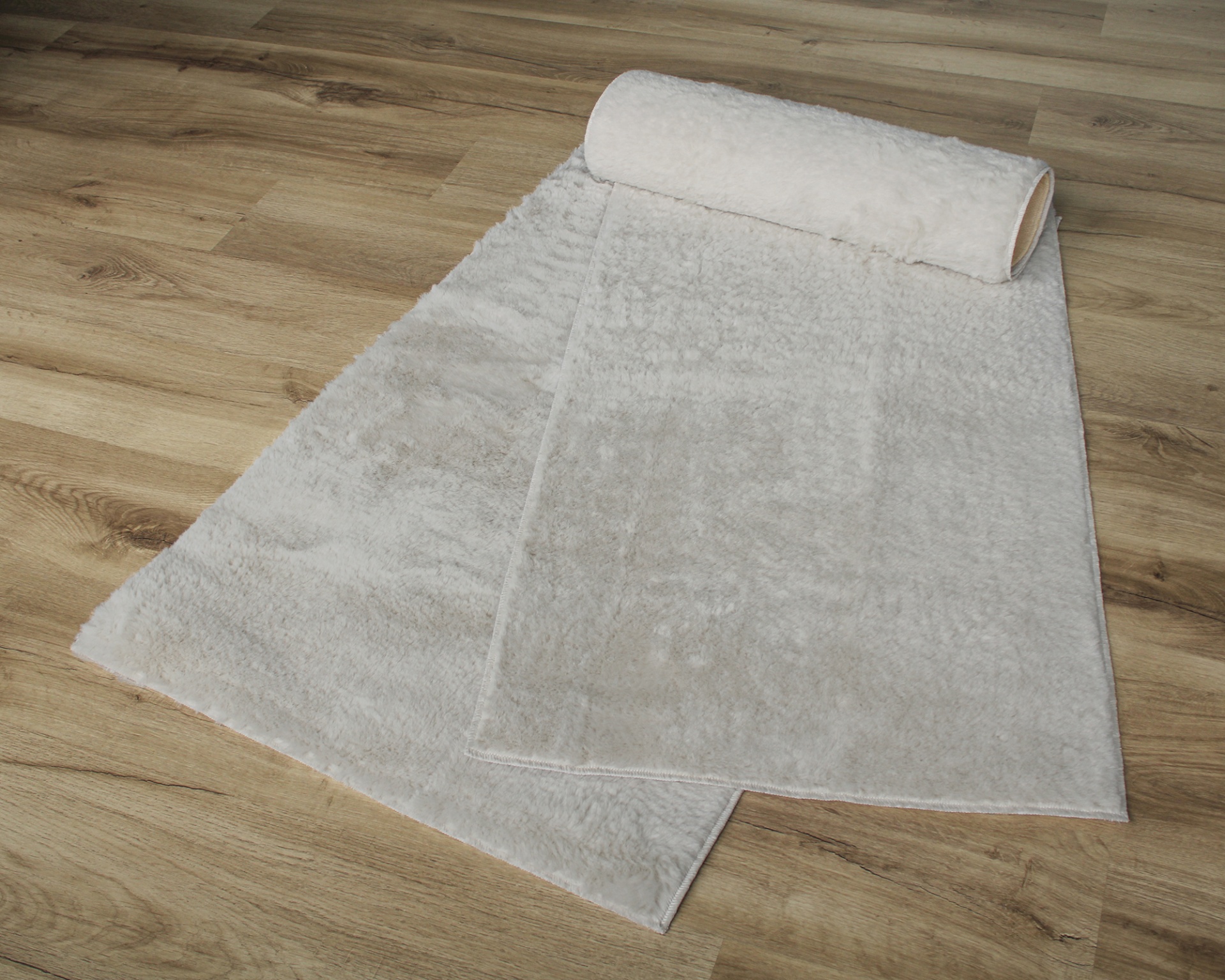 Tapete felpudo branco parcialmente enrolado em chão de madeira clara