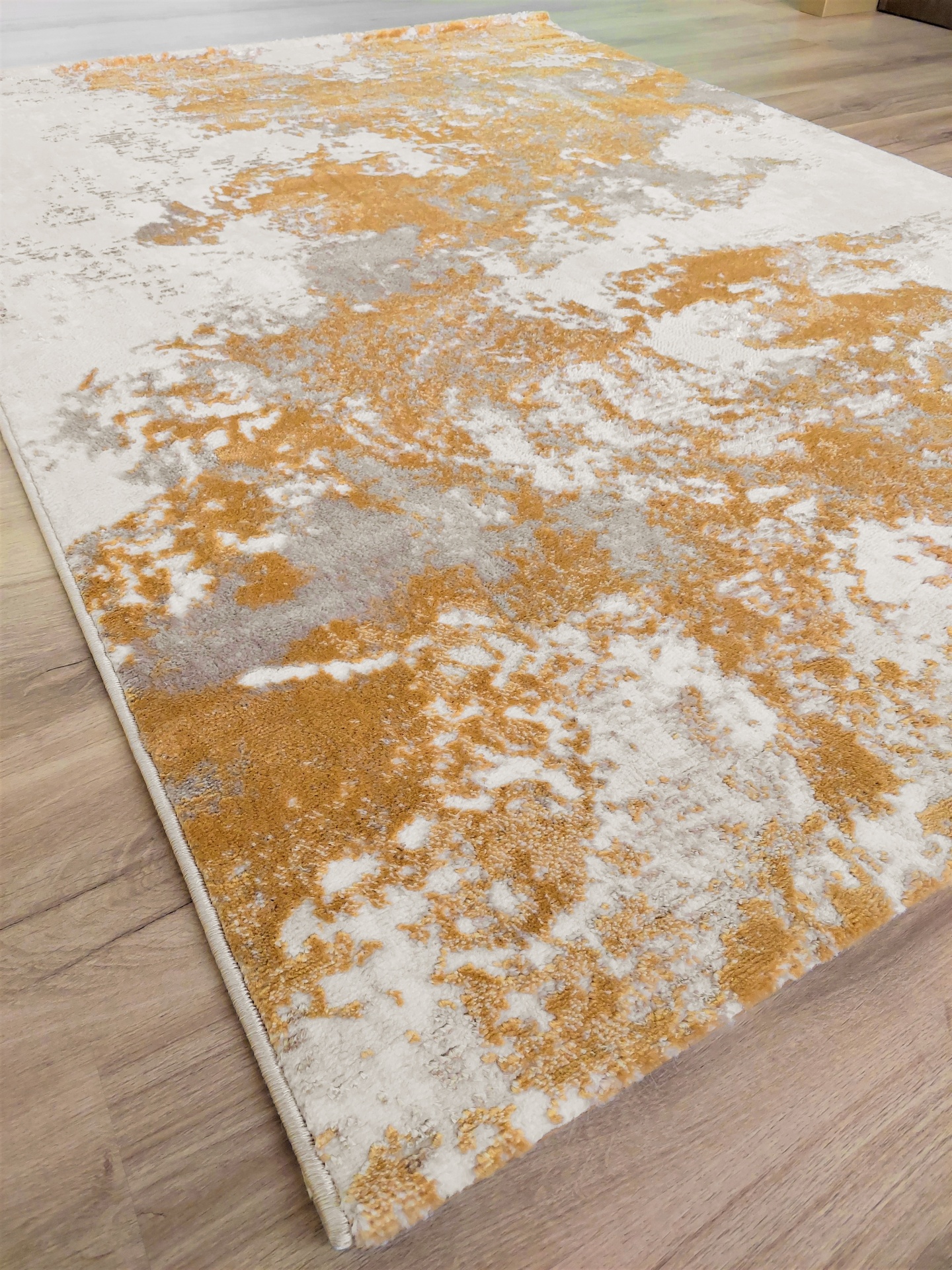 Tapete texturado abstrato branco, bege e dourado sobre chão de madeira