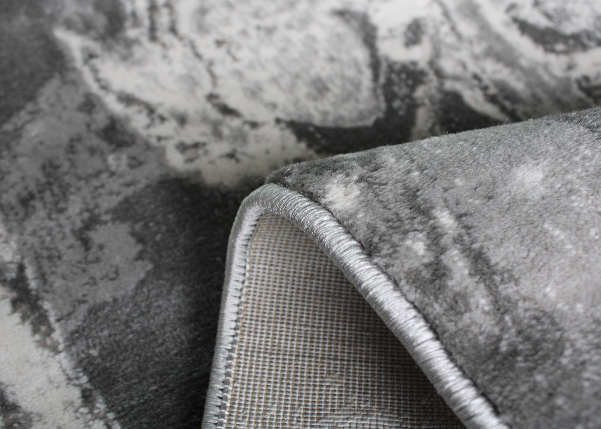 Tapete cinza com padrão abstrato e bordas costuradas