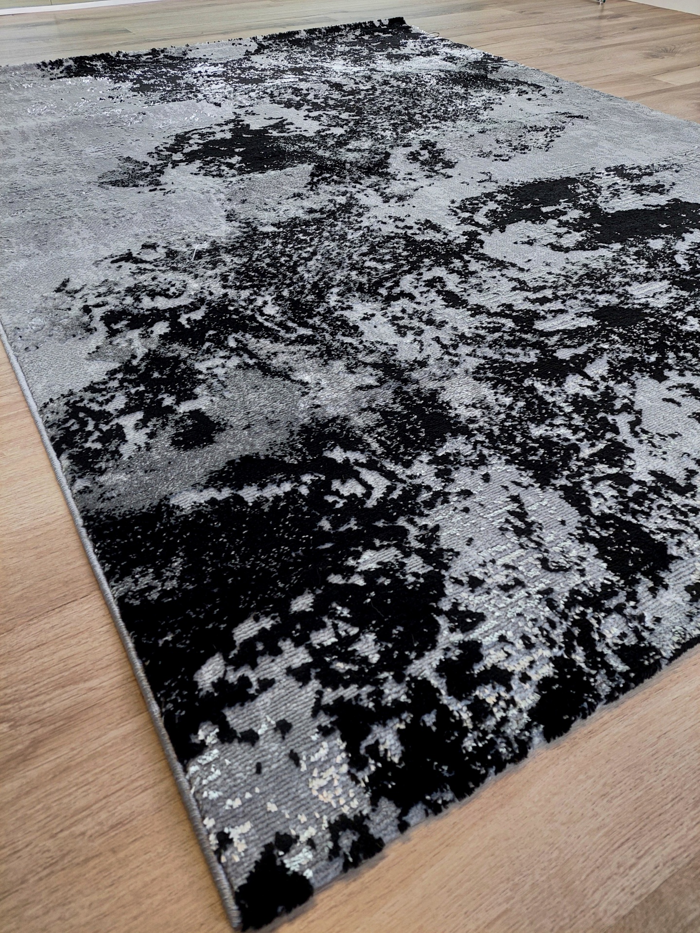 Tapete cinza e preto com padrão abstrato sobre chão de madeira