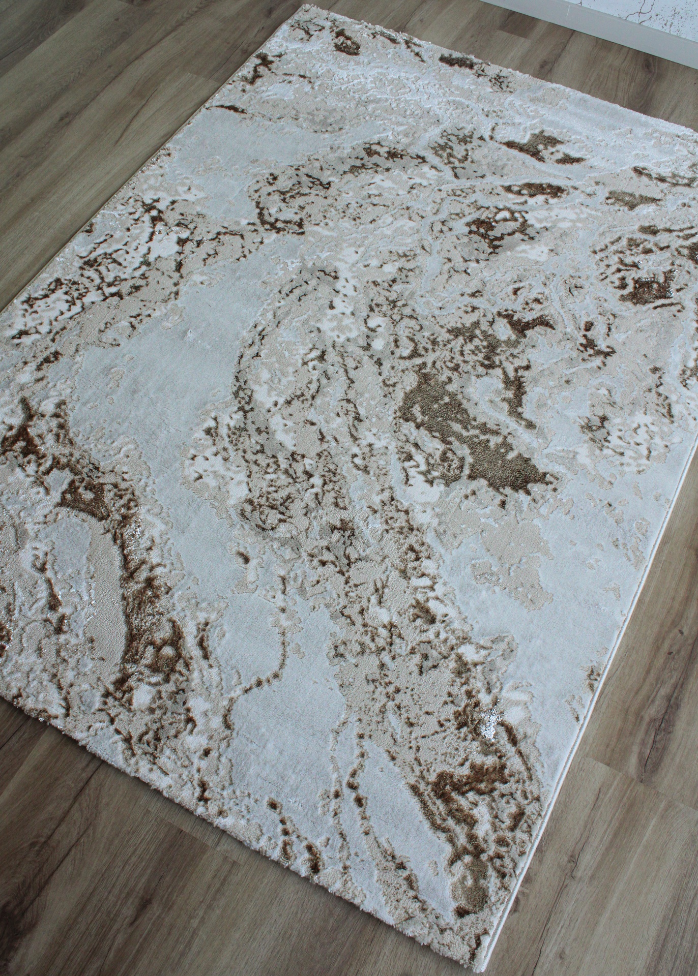 Tapete retangular abstrato em tons de bege e castanho sobre chão de madeira clara