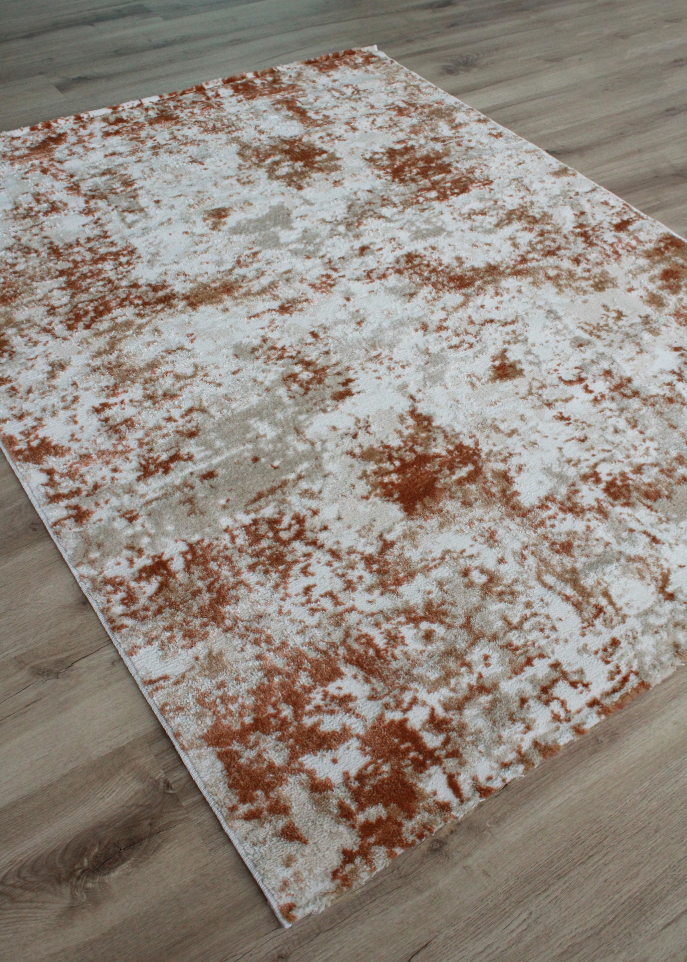 Tapete retangular em padrão abstrato branco, cinza e laranja sobre chão de madeira clara