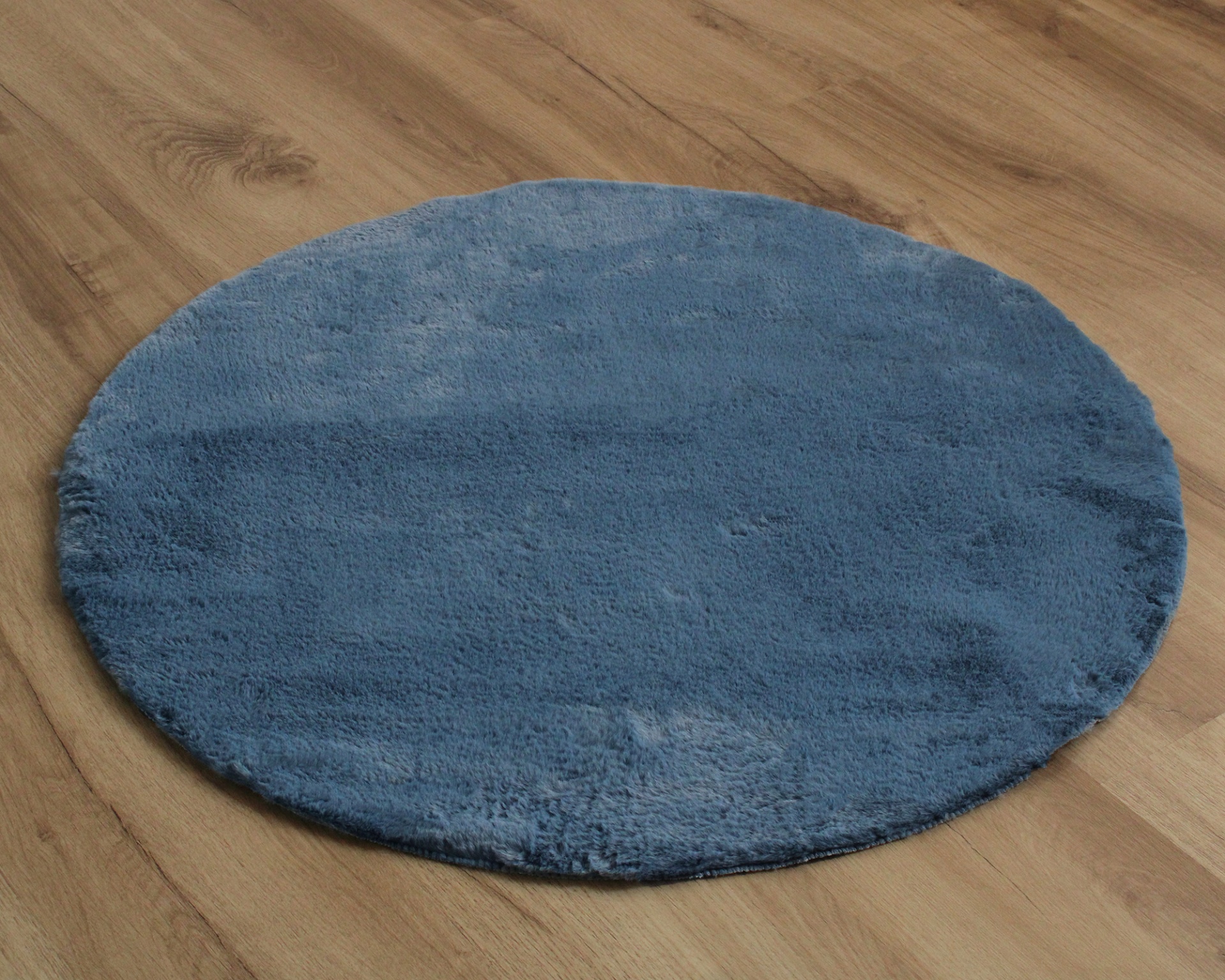 Tapete redondo azul de pelo curto numa superfície de madeira clara