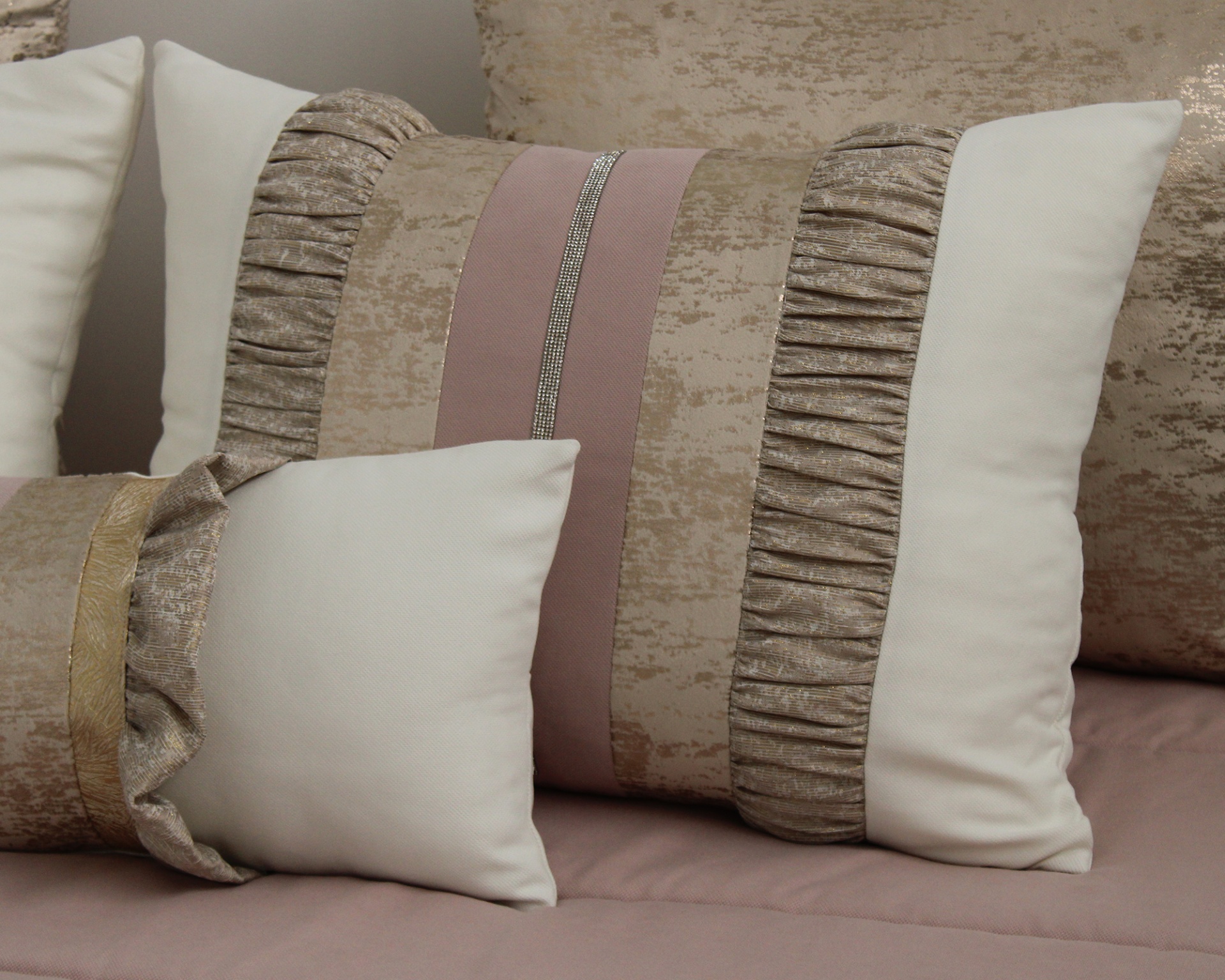 Almofadas decorativas em tons neutros com detalhes em riscas douradas e rosa, texturas aveludadas e frisadas