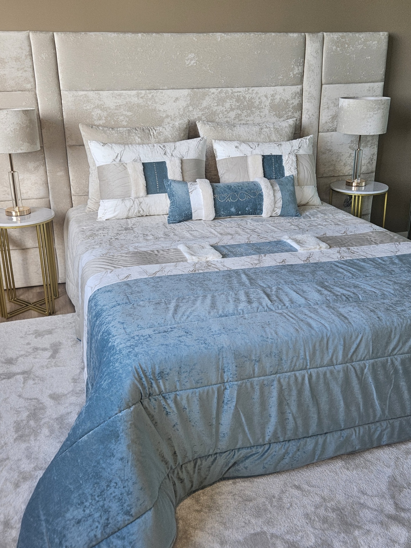 Edredão em Veludo Ref: Nepal Verde Cama estofada com colcha azul e branca e almofadas decorativas, com duas mesas de cabeceira e candeeiros