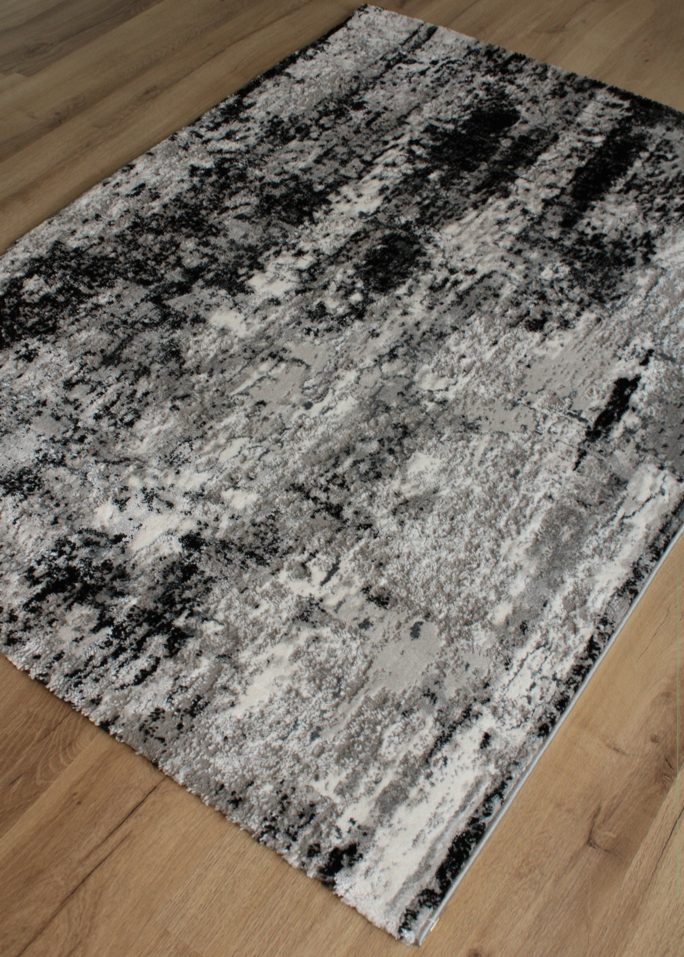 Tapete com padrão abstrato cinza, branco e preto sobre chão de madeira clara