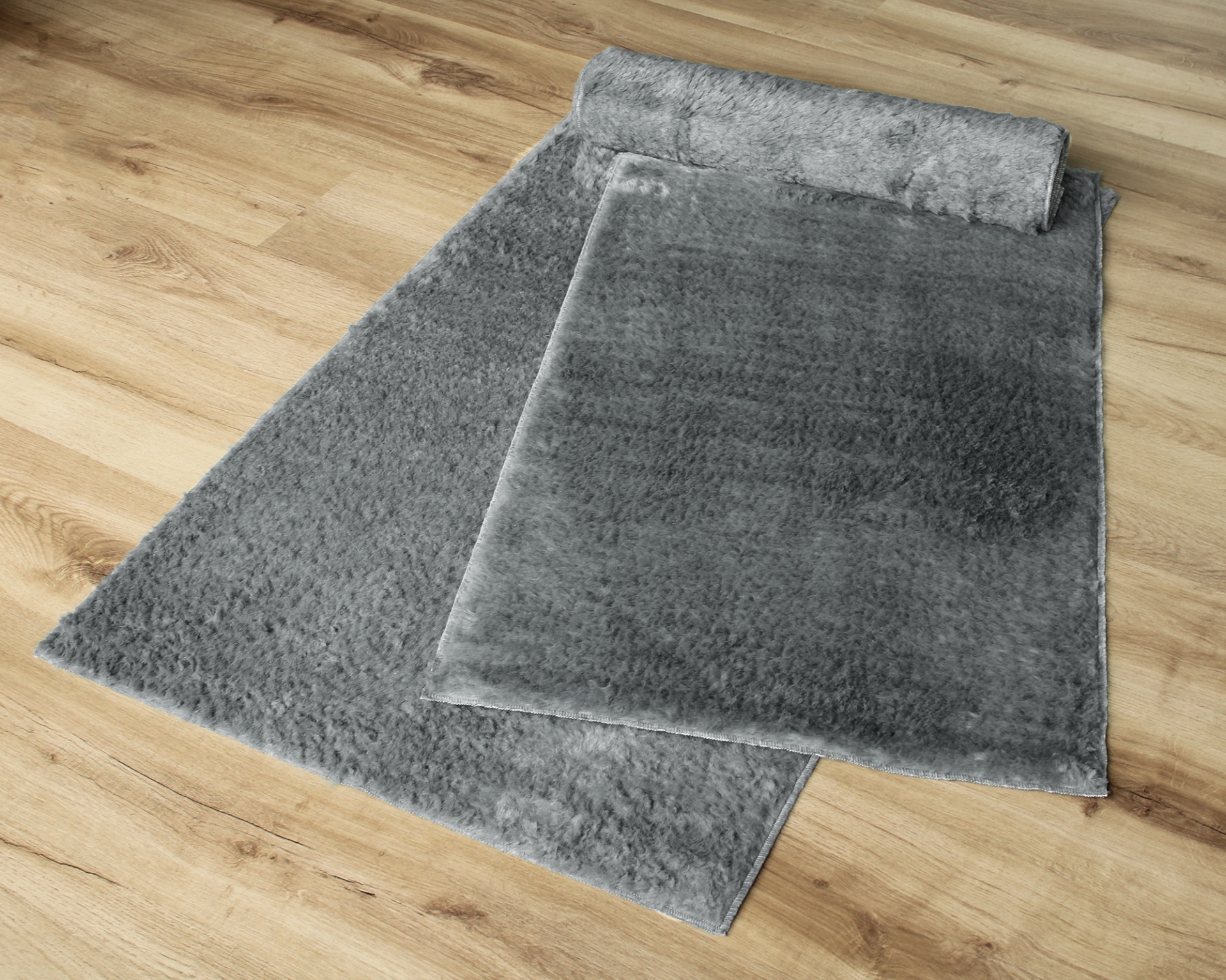 Tapete cinza felpudo parcialmente enrolado em chão de madeira clara