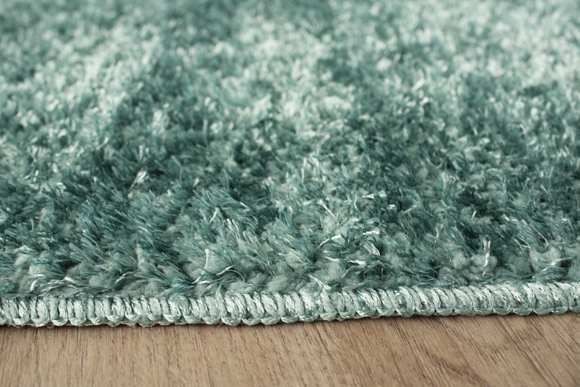 Tapete verde felpudo com borda costurada sobre chão de madeira clara