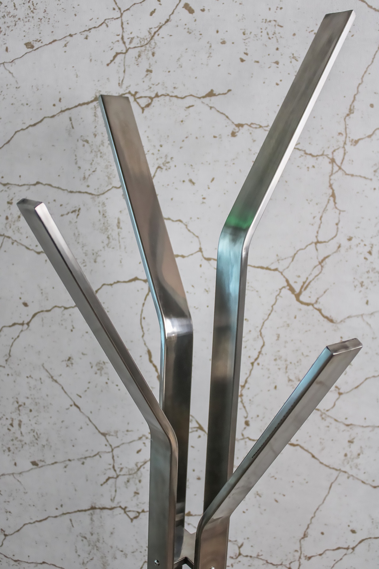 Cabide de pé metálico prateado com quatro ganchos, fundo branco com veios cinzentos