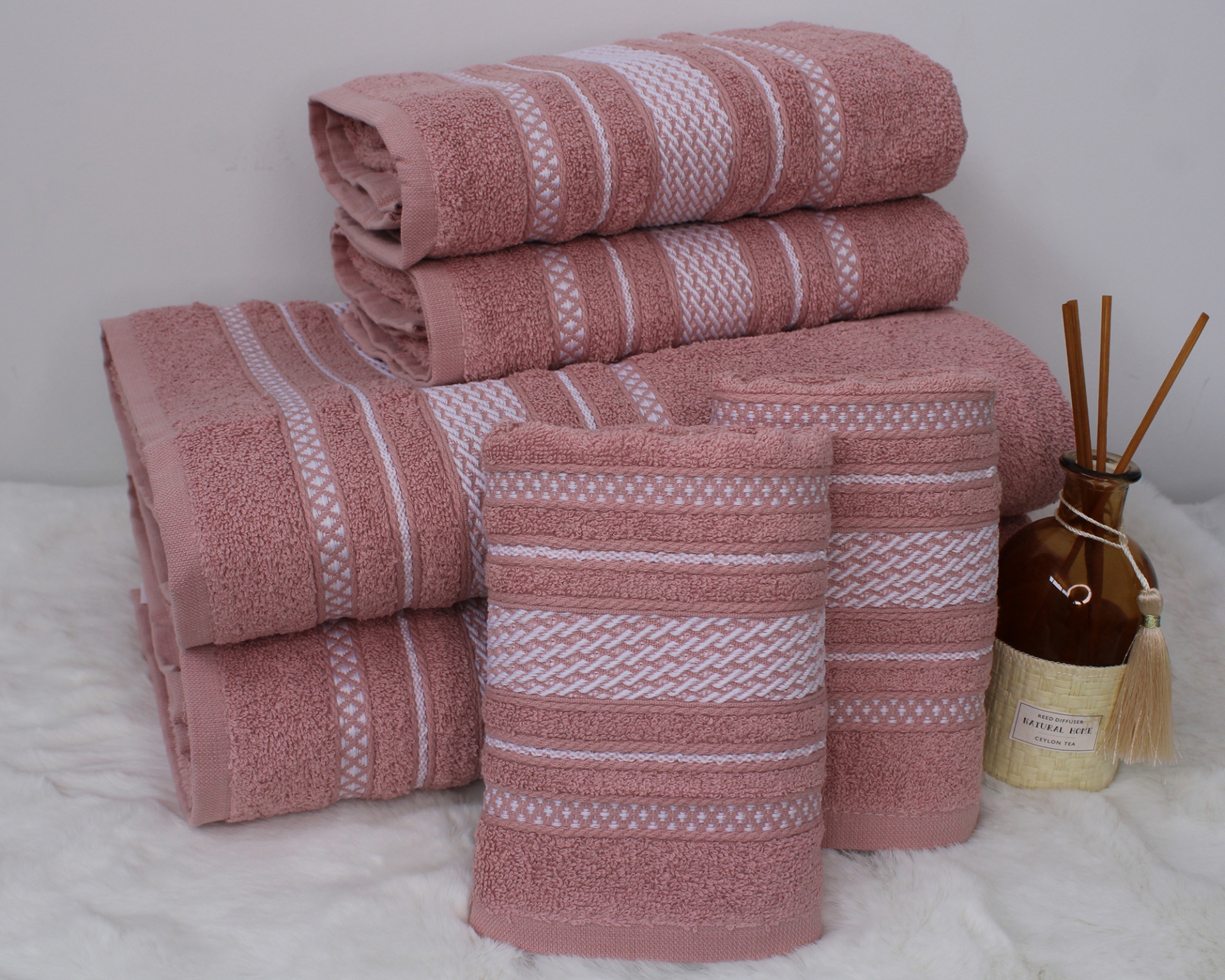 Conjunto de toalhas rosa com riscas brancas e difusor de aromas castanho ao lado