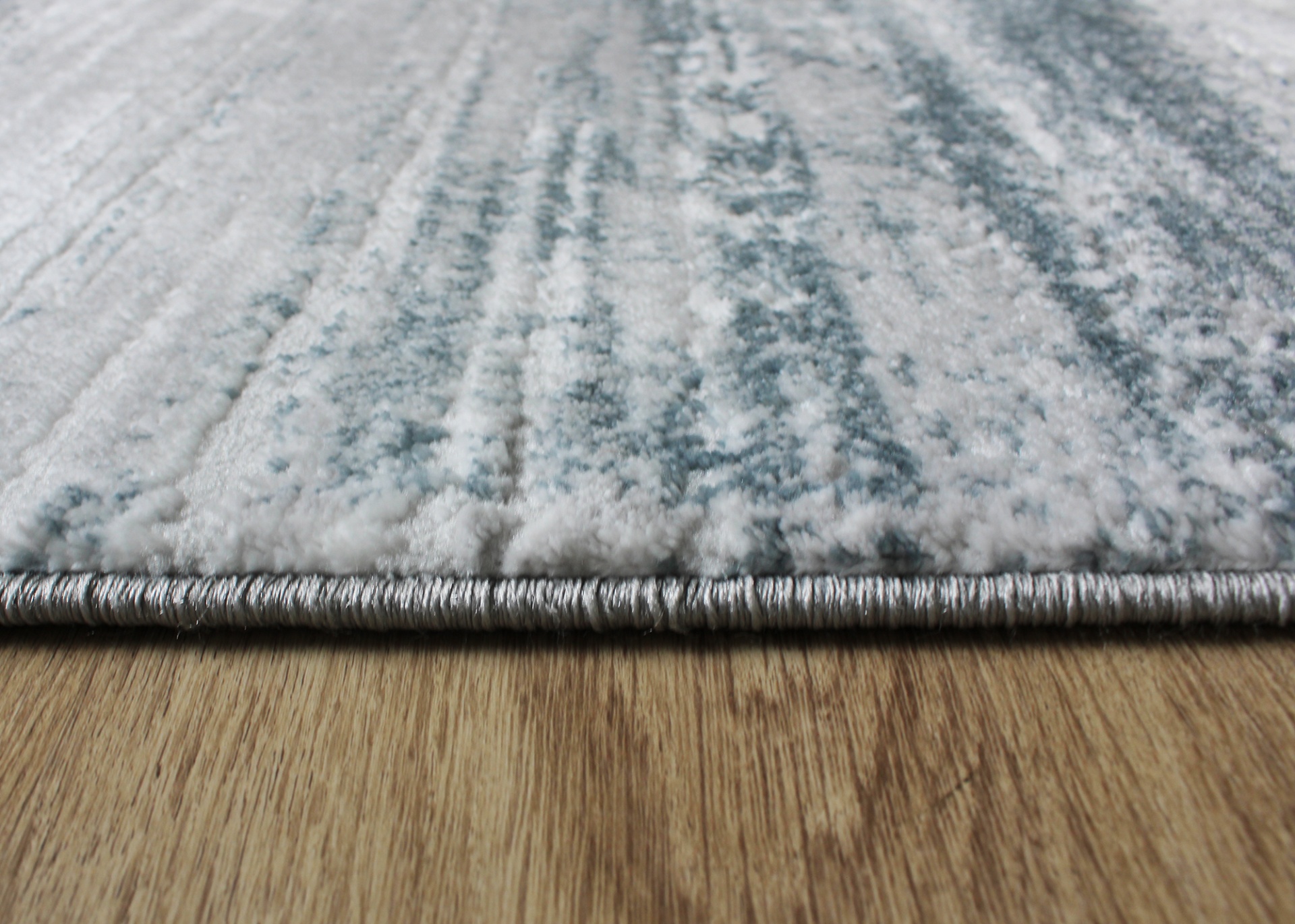 Tapete cinza e branco com borda cinza sobre chão de madeira