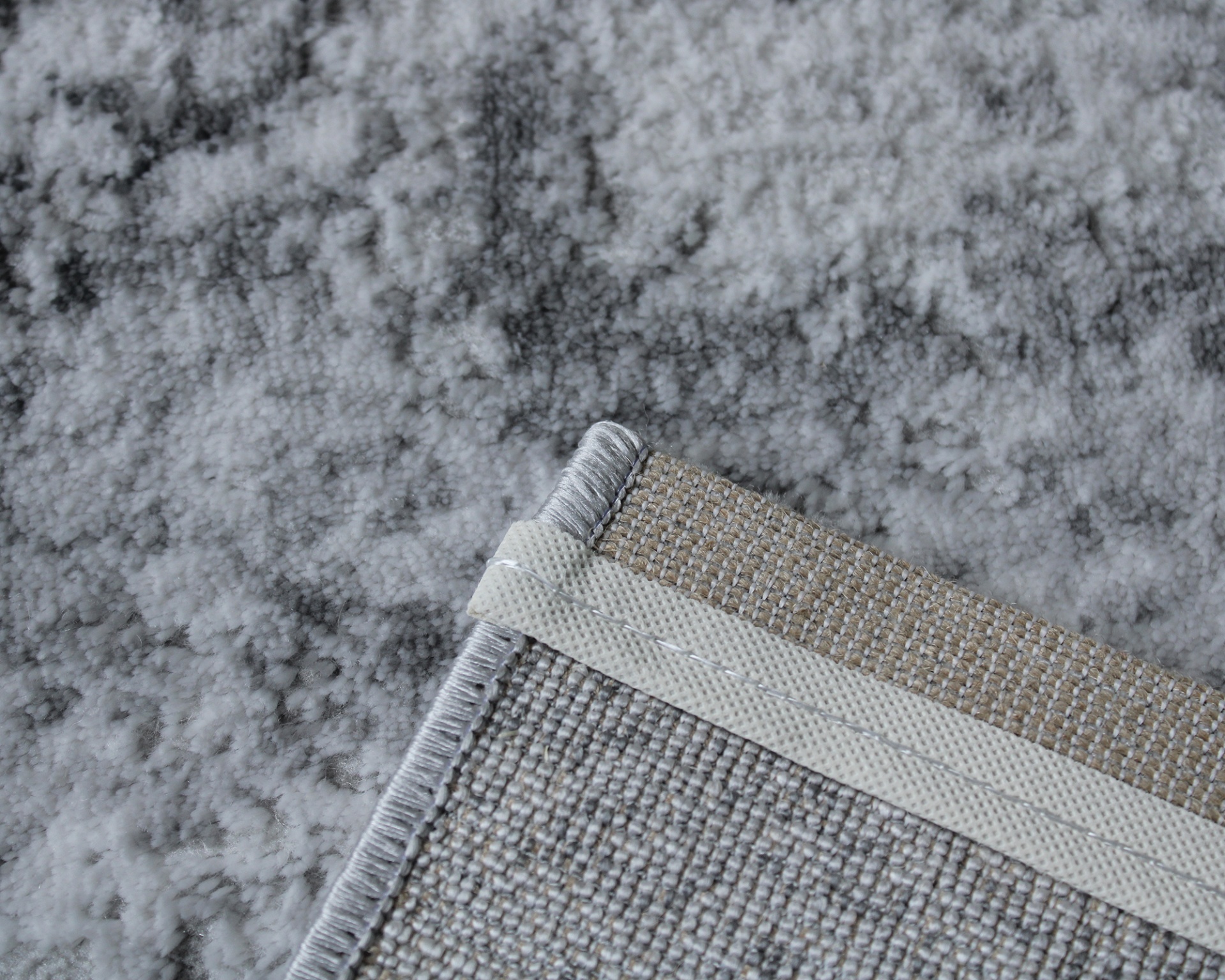 Tapete cinzento com padrão abstrato e bordas costuradas em vista detalhada