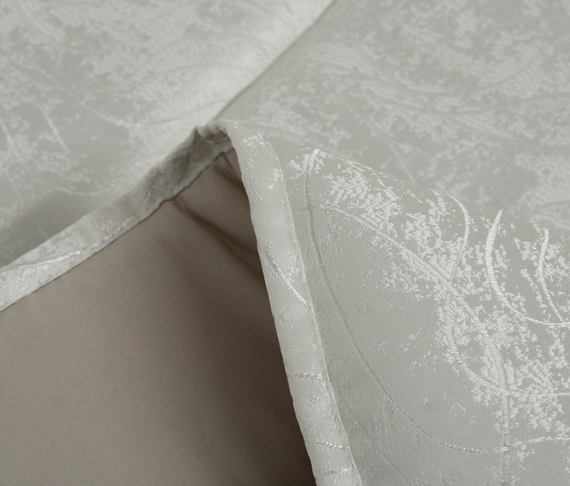 Tecido branco com padrão floral em relevo e acabamento costurado