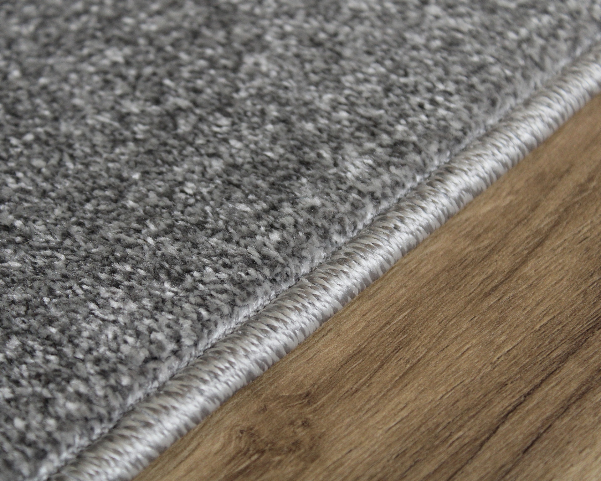 Tapete cinzento felpudo com borda enrolada sobre chão de madeira