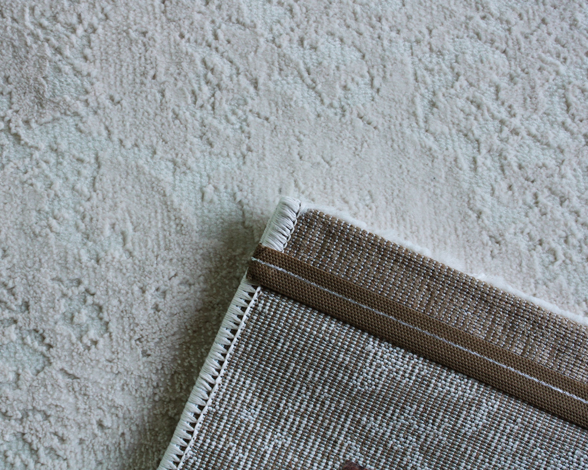 Tapete tecido bege com borda castanha sobre tapete felpudo claro com padrão