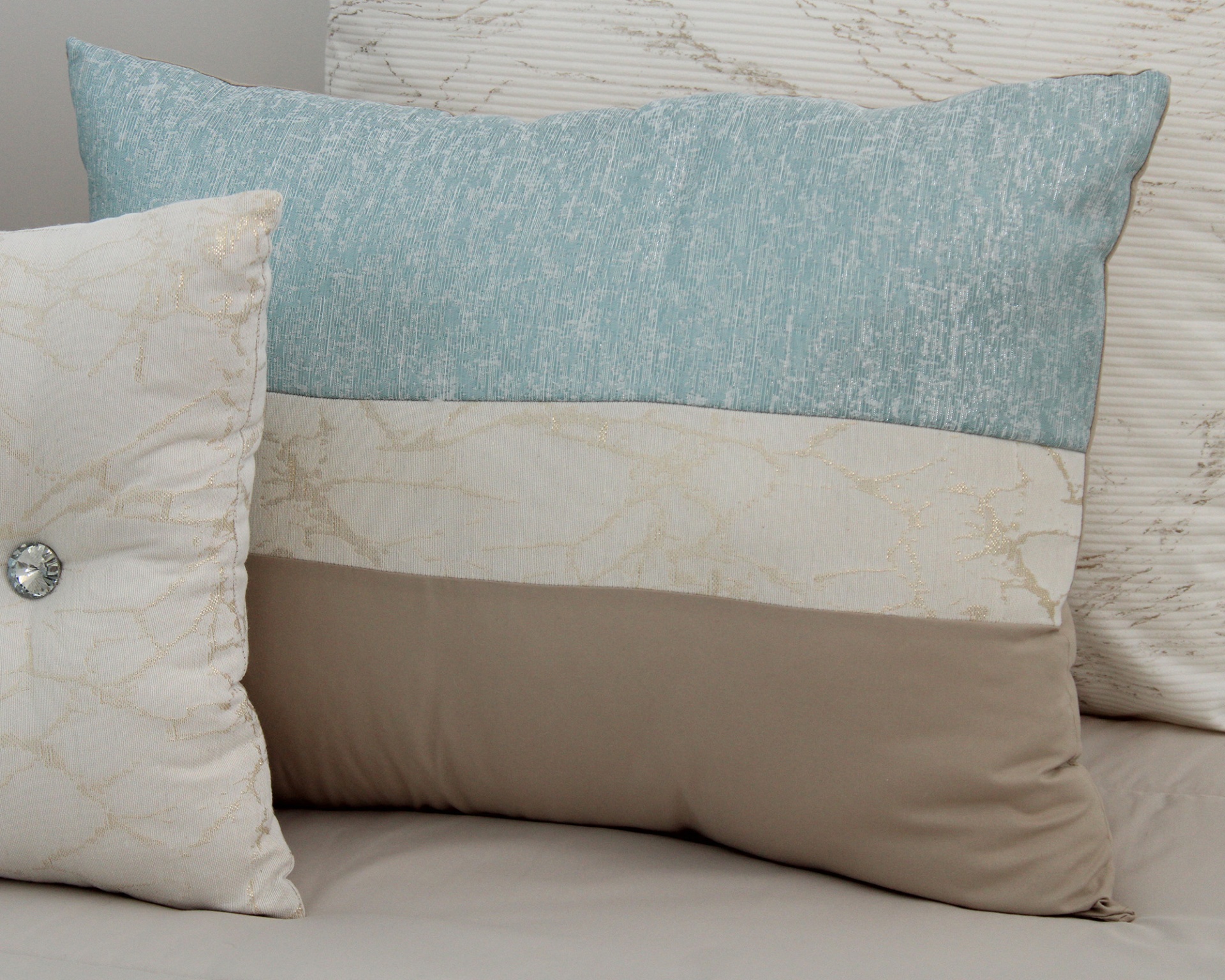 Conjunto de três almofadas decorativas em tons azul, bege e castanho claro sobre sofá.