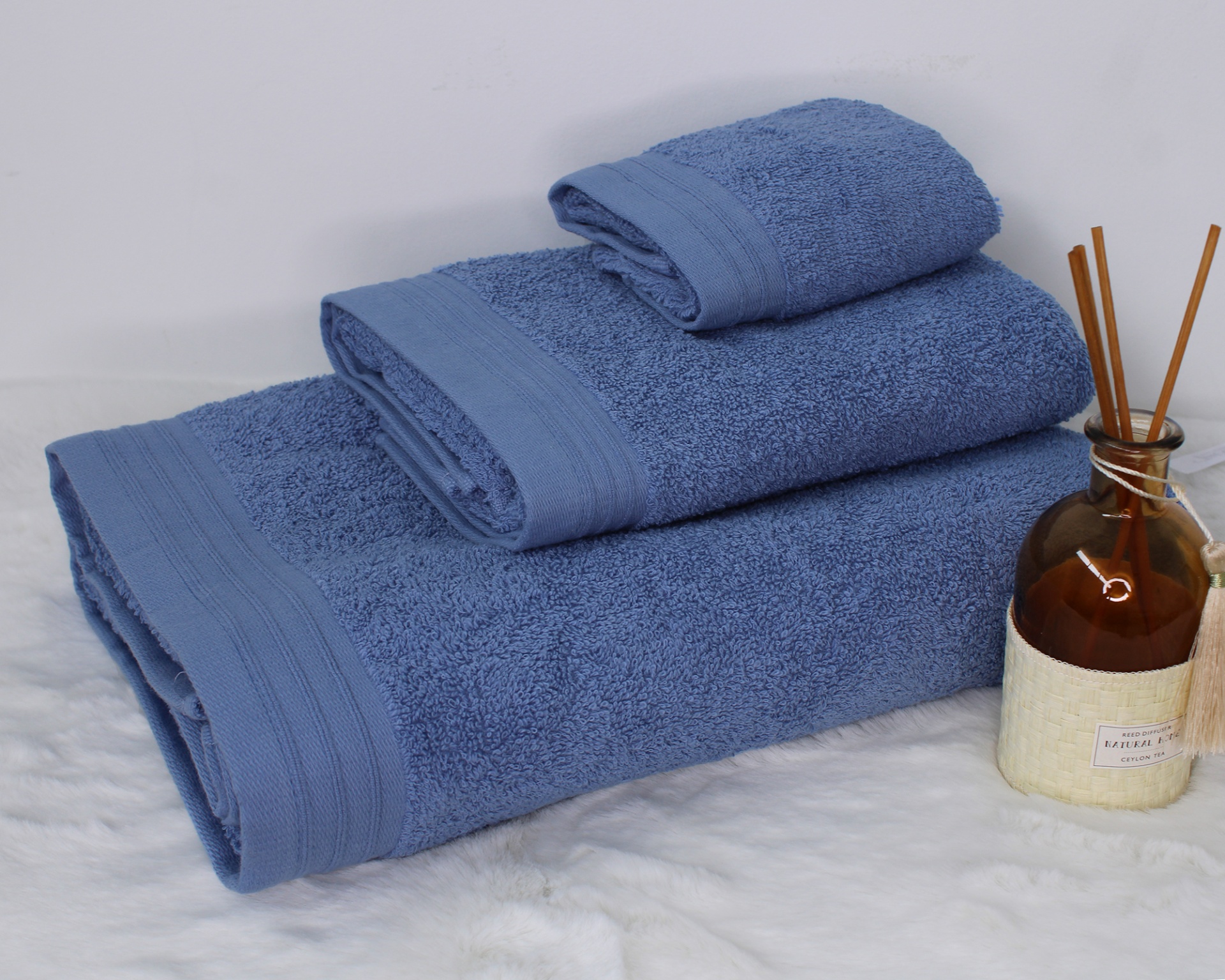 Conjunto de toalhas azuis empilhadas com frasco de aroma ao lado
