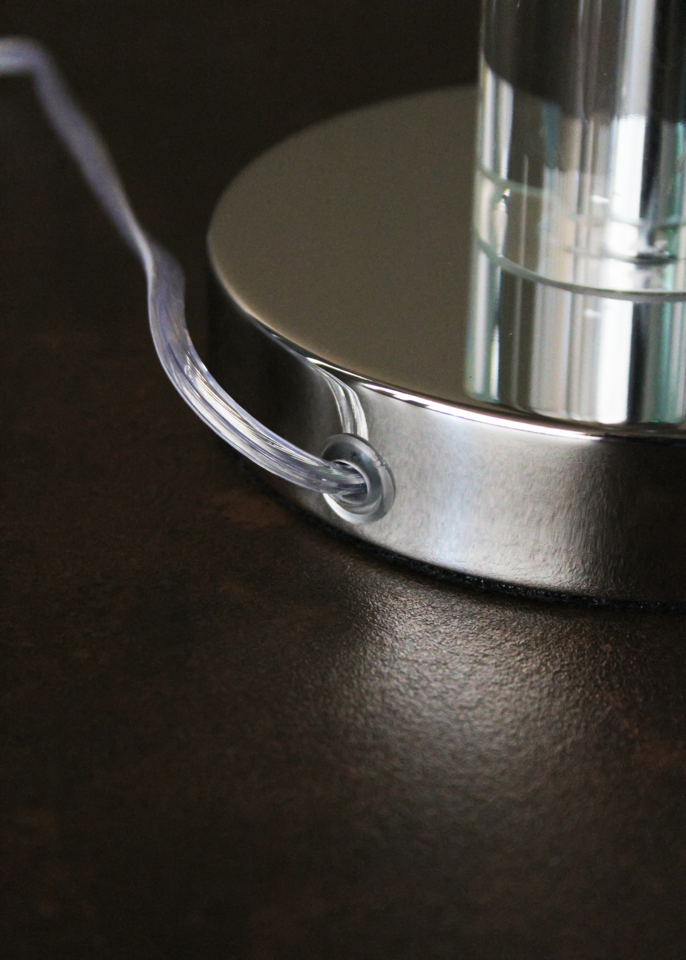 Base metálica redonda prateada com cabo transparente numa superfície escura.