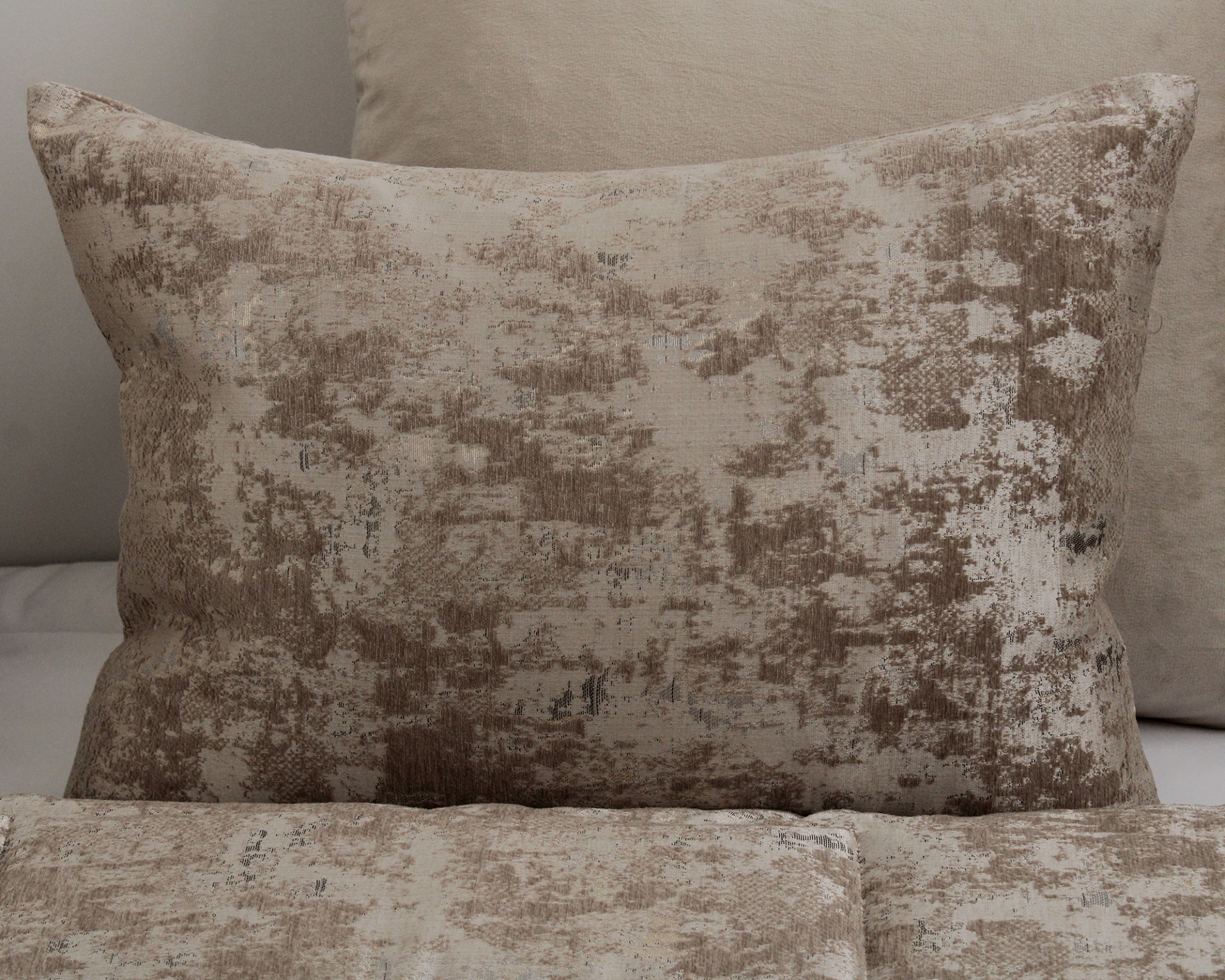 Três almofadas retangulares em tons de bege com padrão texturizado abstrato