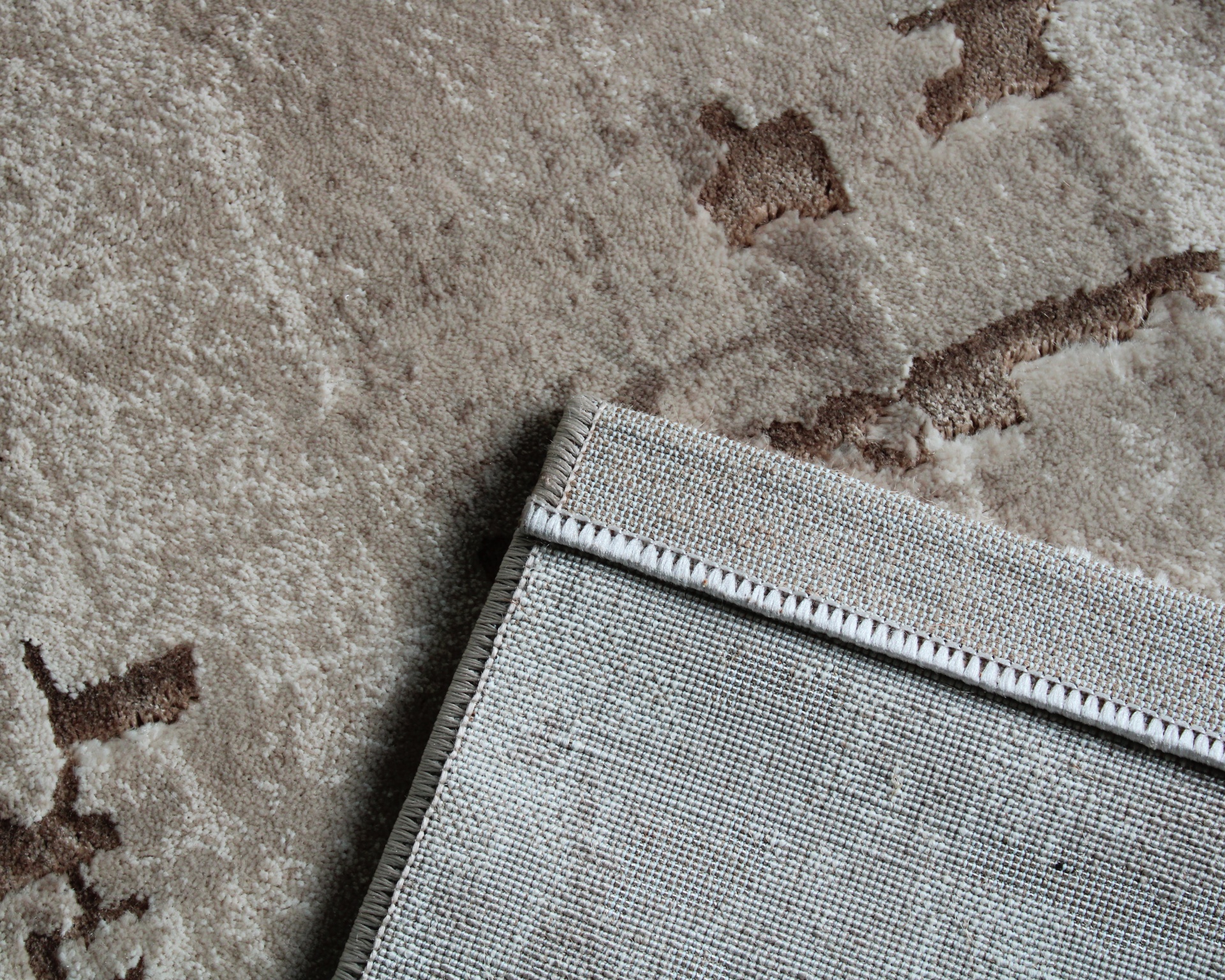 Tapete castanho claro com padrão e dobra mostrando o verso em tecido grosso.