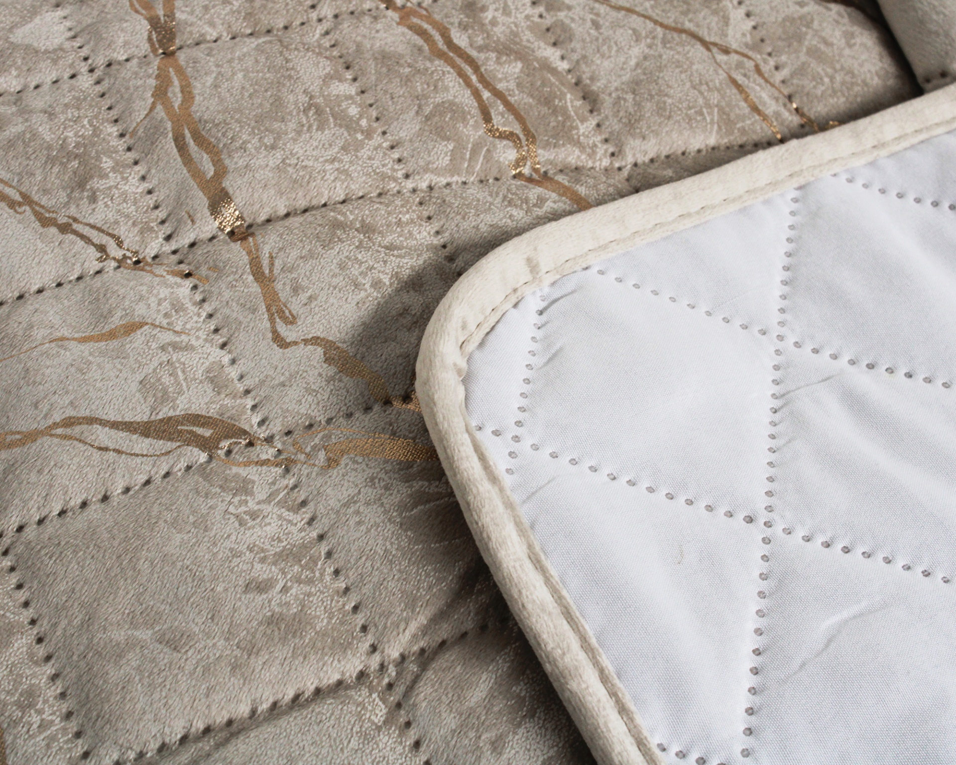 Colchão cinzento com padrão dourado e tapete branco bordado no canto