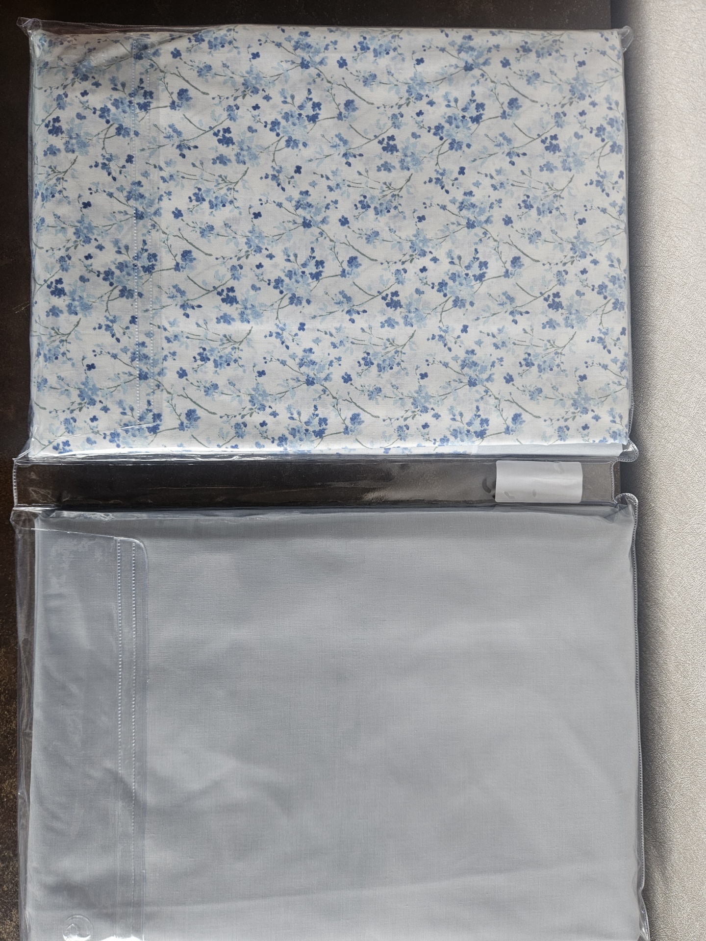 Conjunto de roupa de cama com padrão floral azul e lençol azul claro embalados em plástico.