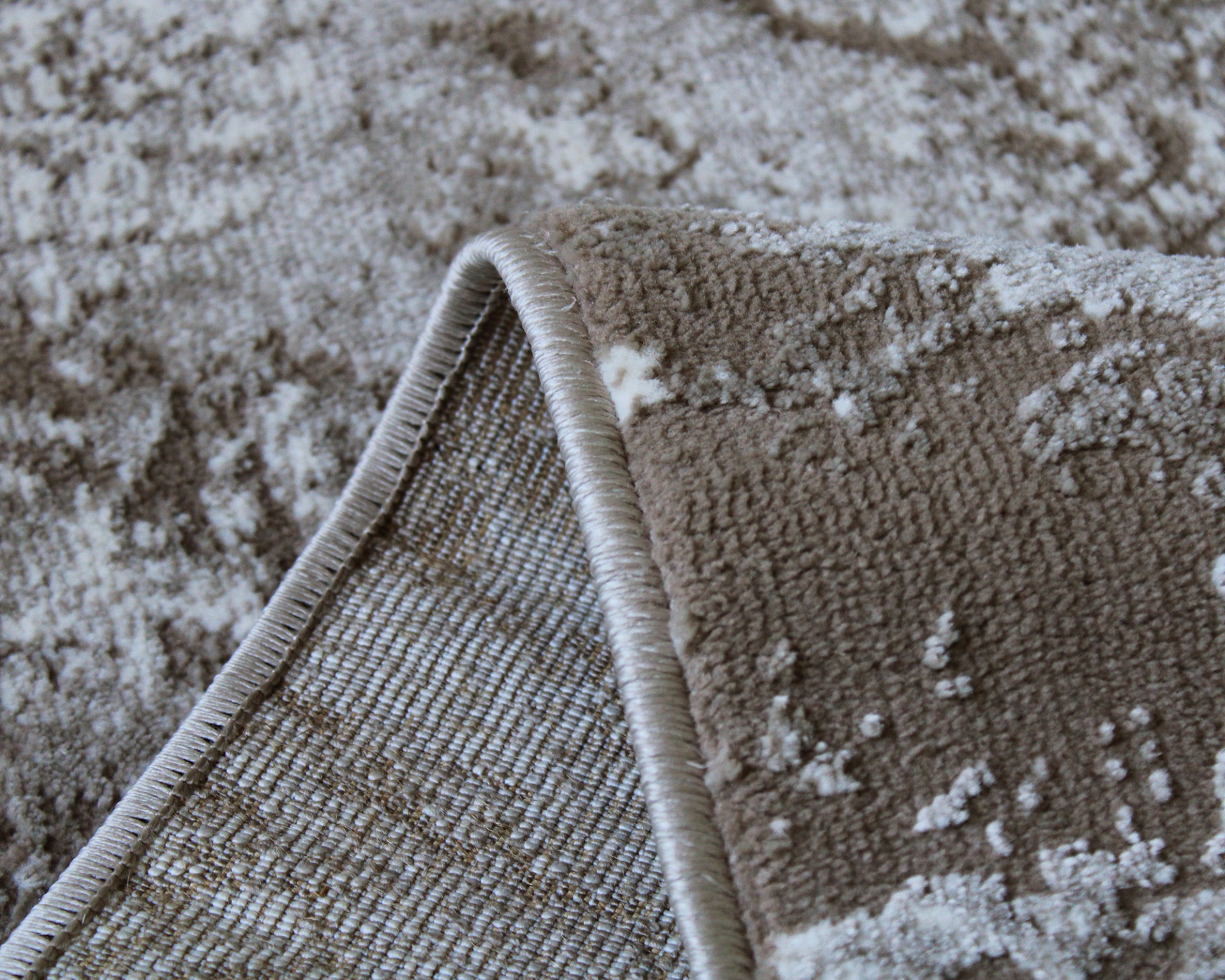 Tapete castanho com padrão abstrato branco e bege, canto dobrado mostrando lado inferior