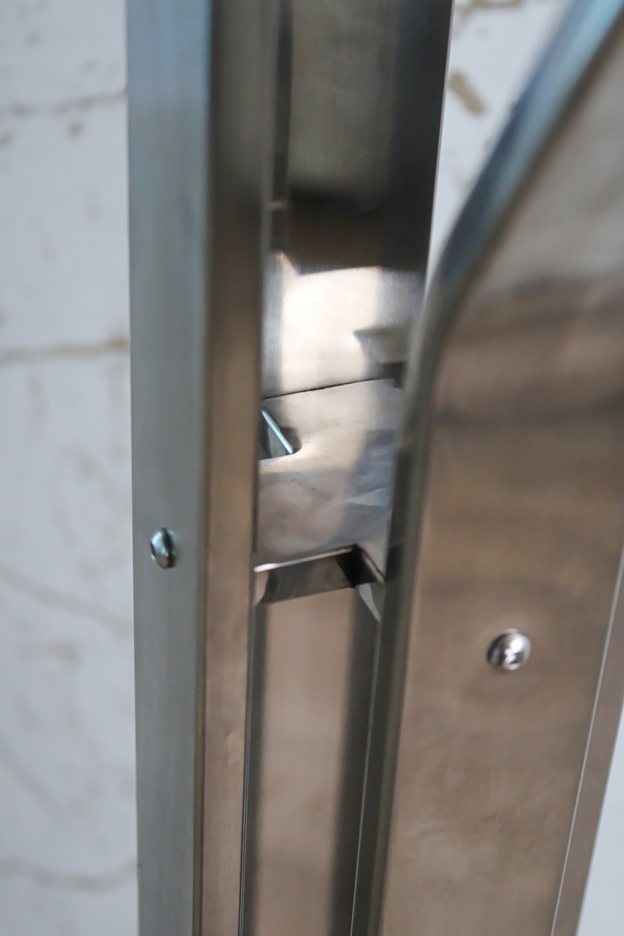 Fechadura metálica prateada embutida numa porta metálica com parafusos visíveis