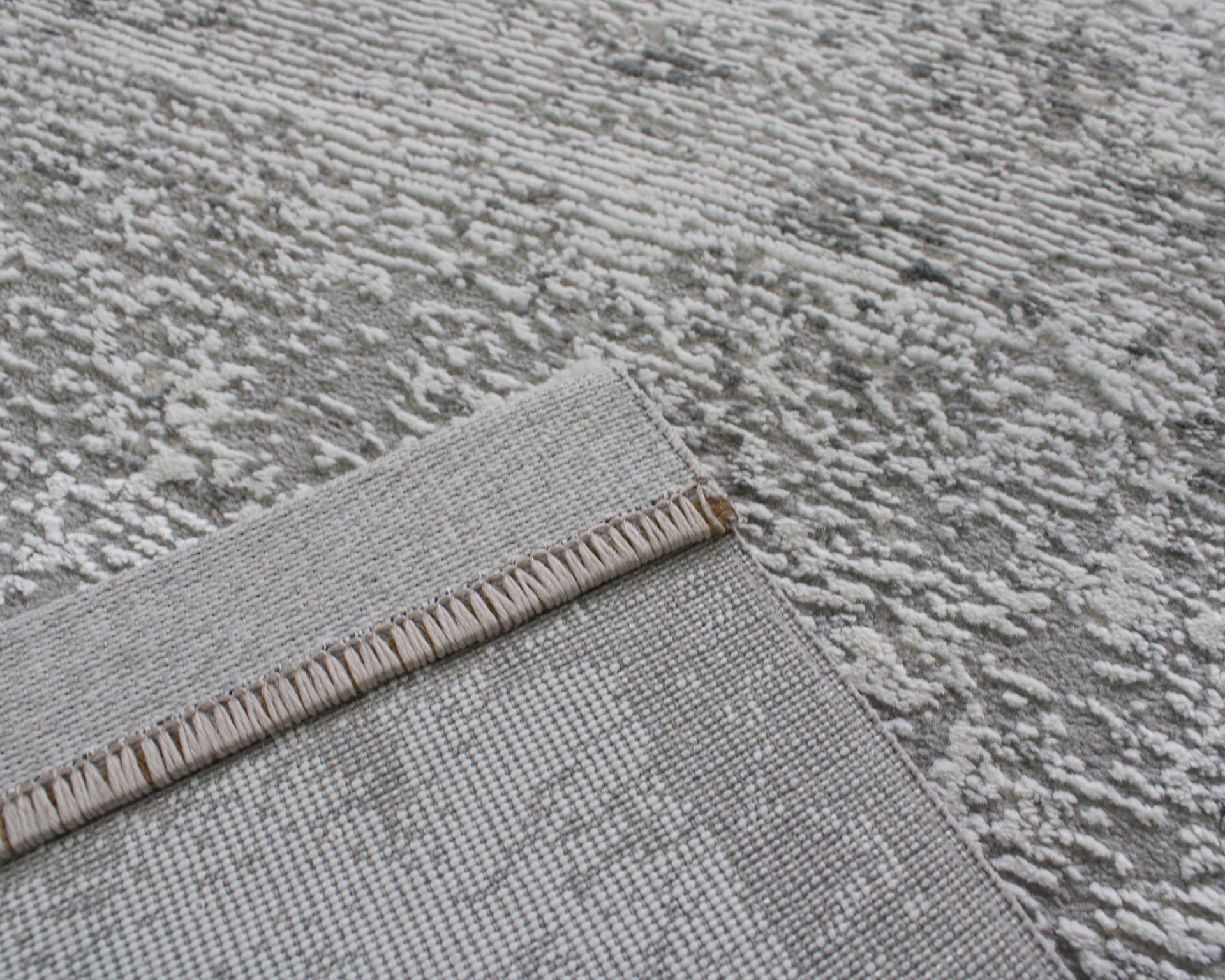 Tapete cinza com padrão texturizado e uma borda dobrada mostrando o verso.