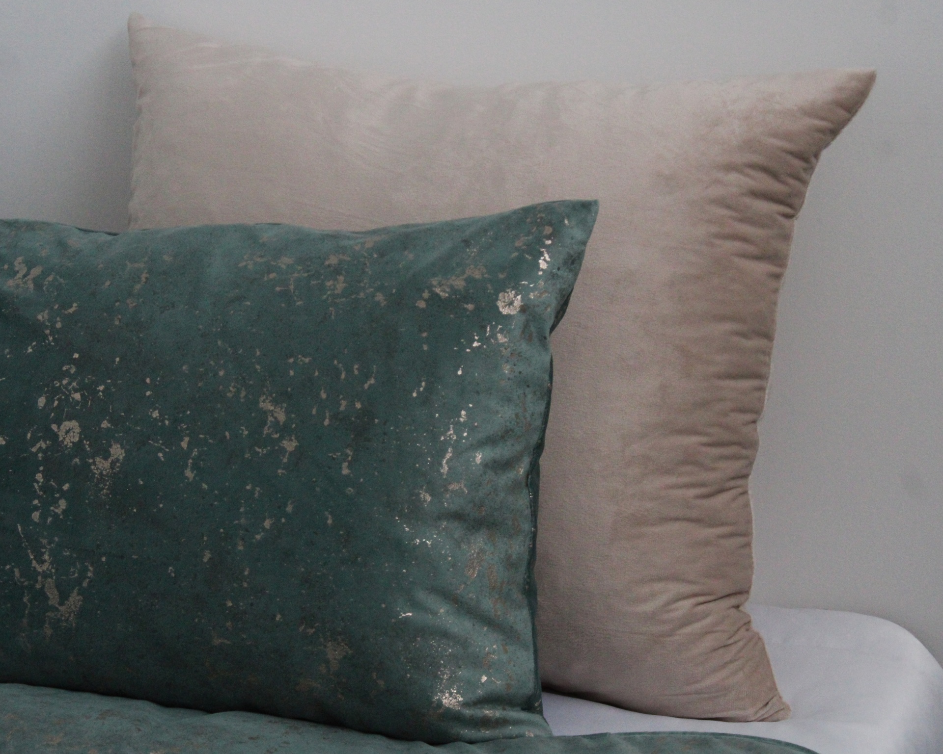 Duas almofadas, uma bege e outra azul turquesa com padrão dourado, numa cama