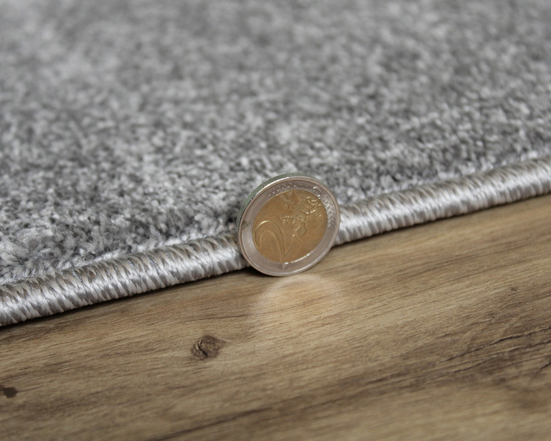 Tapete cinzento claro com moeda de 2 euros e chão de madeira clara