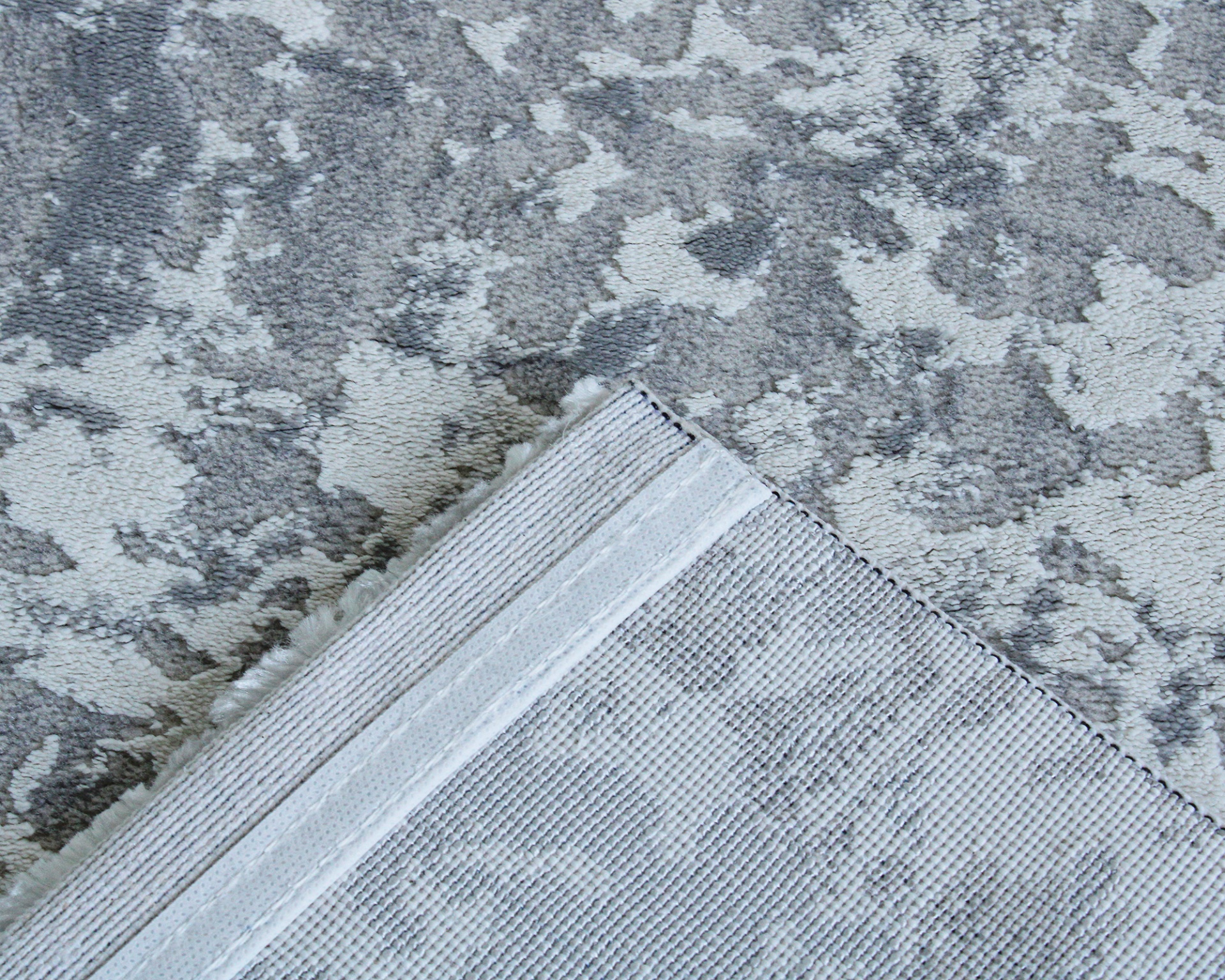 tapete cinzento com padrão abstrato e verso com acabamento em linhas paralelas e franjas