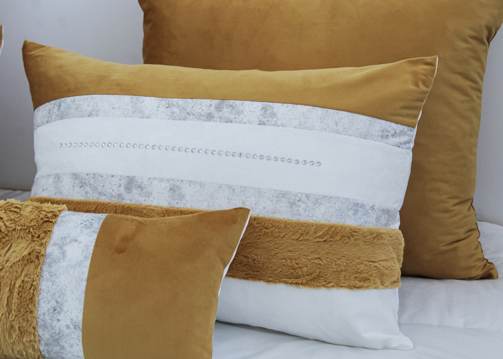 Três almofadas decorativas castanhas e brancas com texturas e cristais sobre cama branca